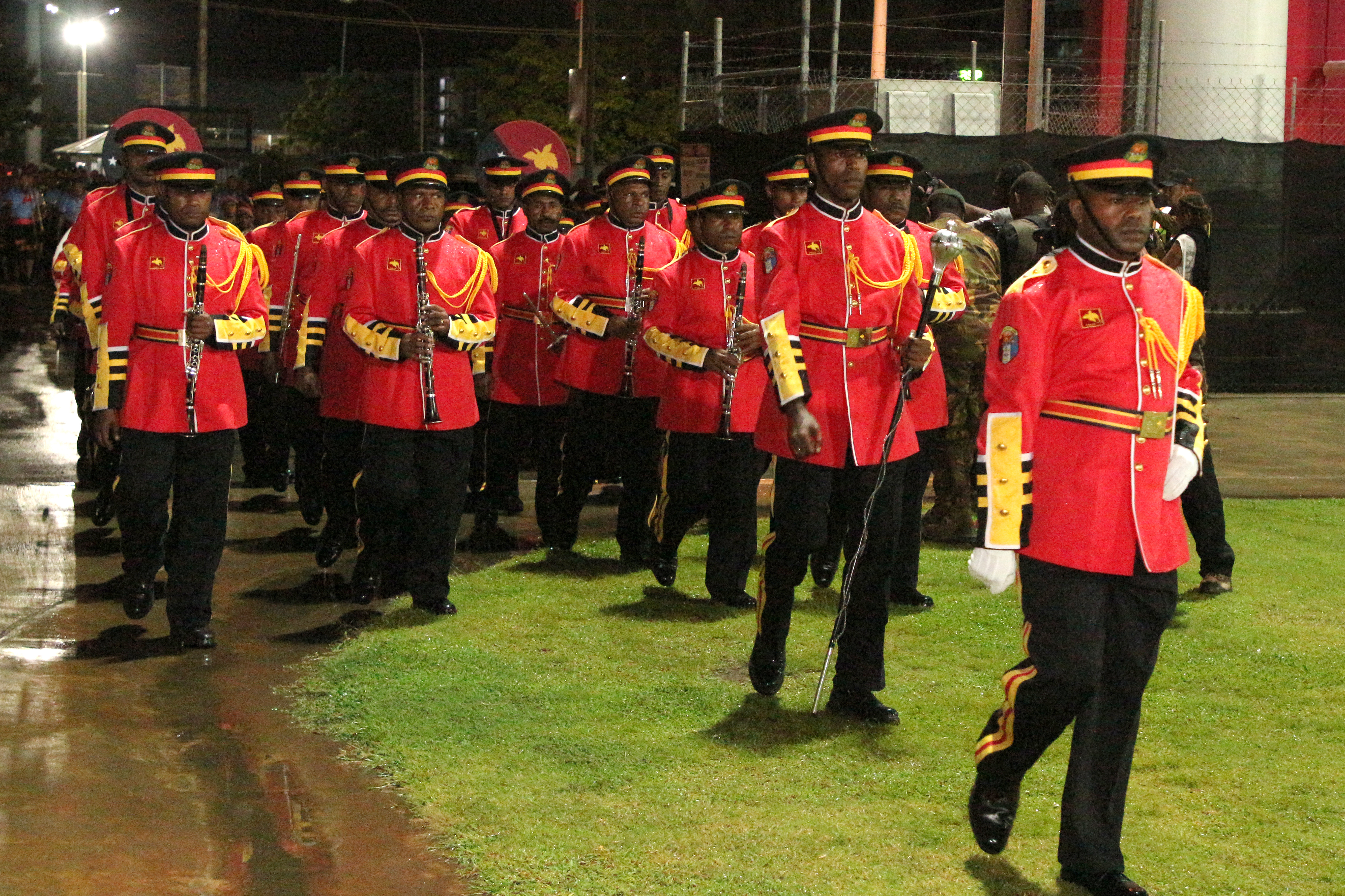 Servicemen in PNG march in a Port Moresby stadium in a ceremony to mark the British king's coronation. They are wearing red tunics and black trousers