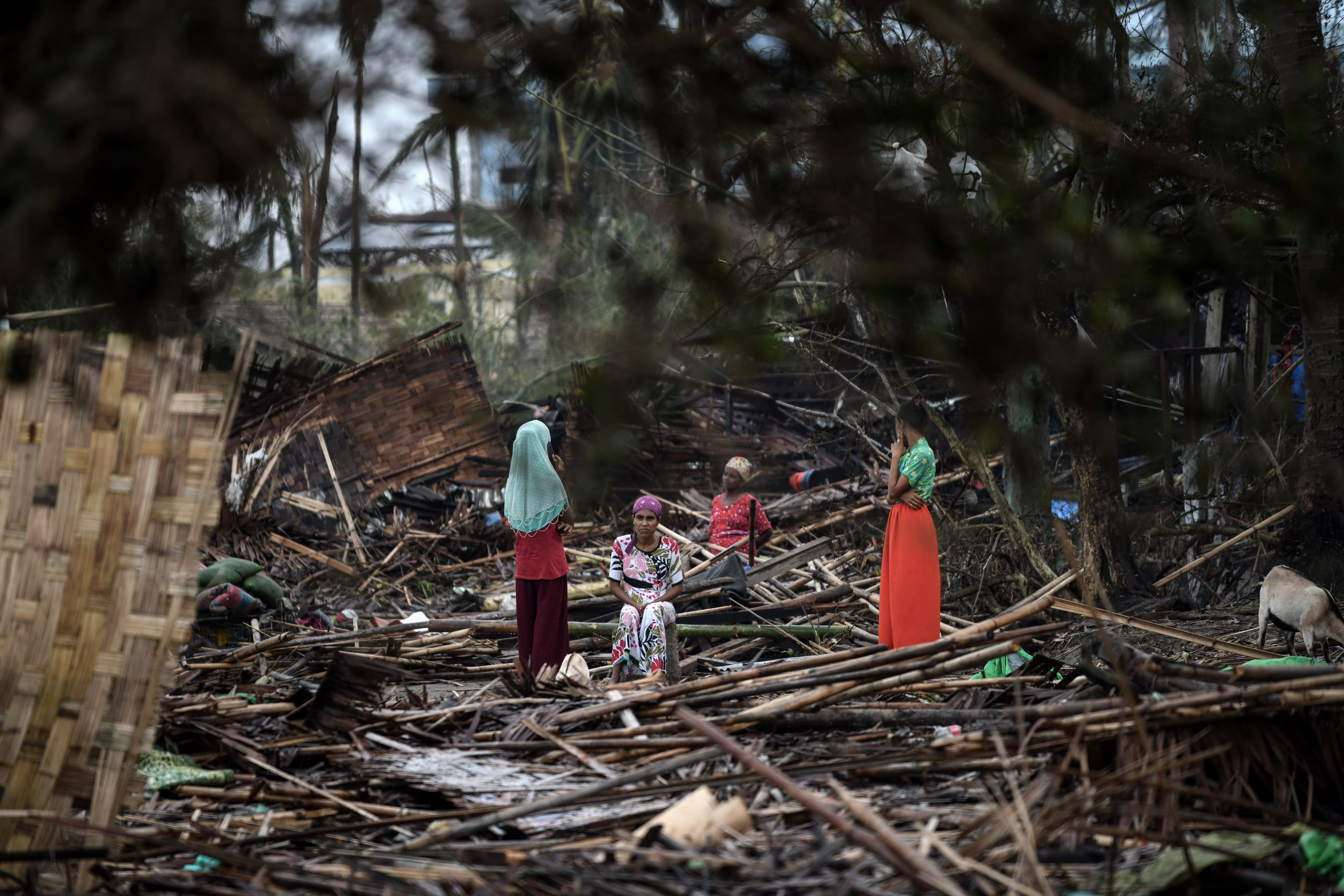 Rohingya women sit and stand in their destroyed house at Basara refugee camp in Sittwe