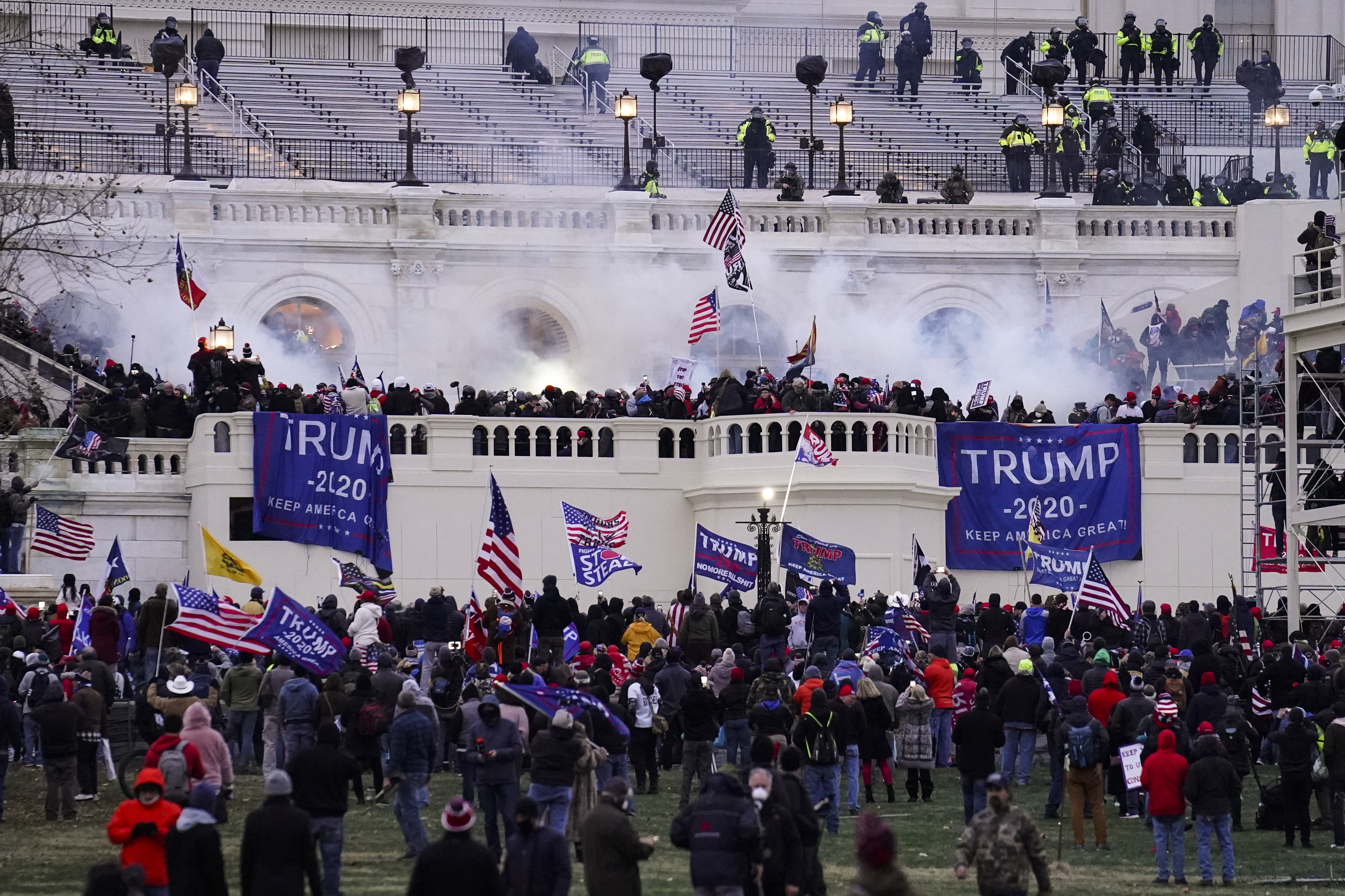 People waving Trump banners and American flags gather before the US Capitol, as smoke and tear gas rise from the riot