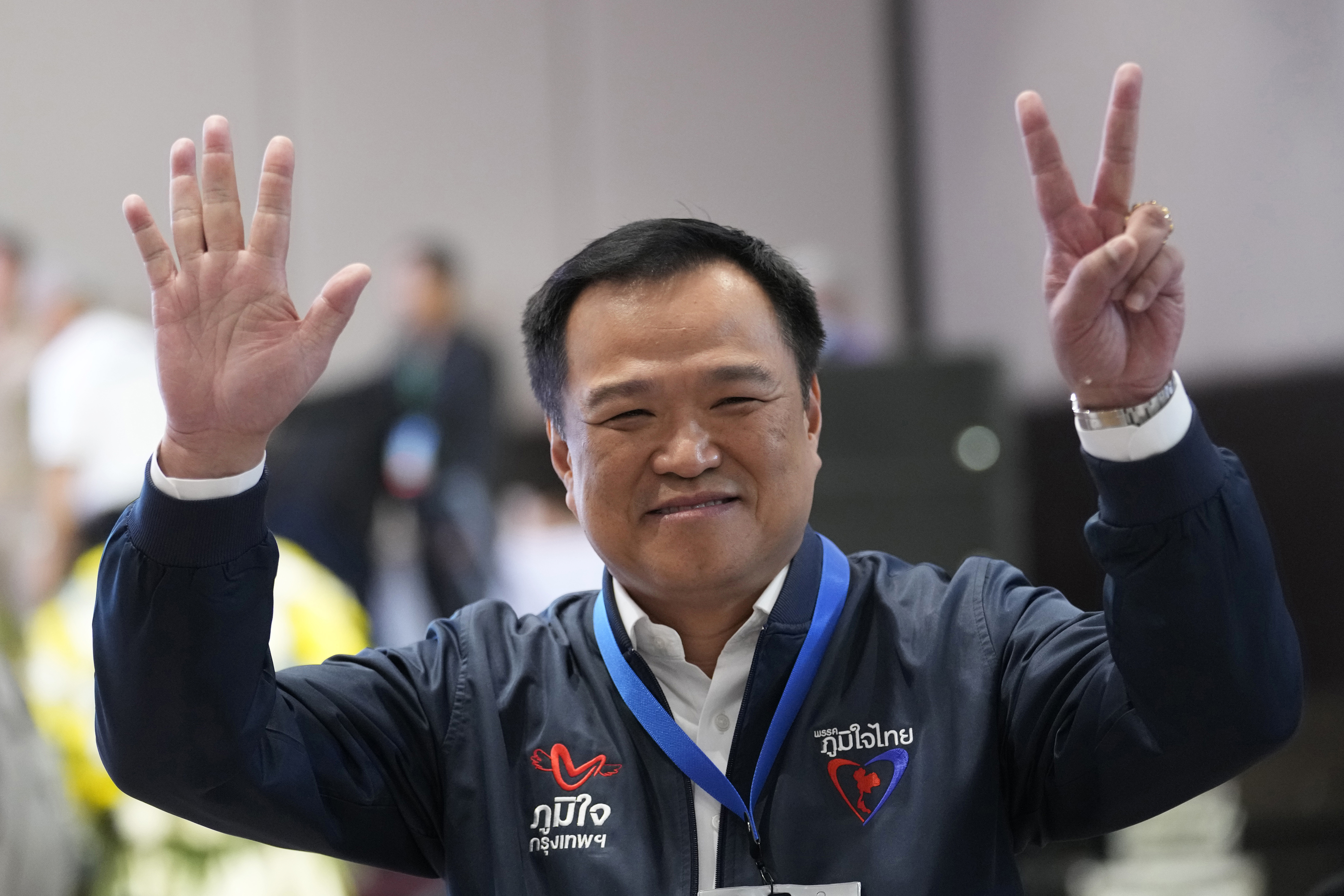 Anutin Charnvirakul holding up his hands. He is wearing a blue bomber jacket and looks relaxed. 