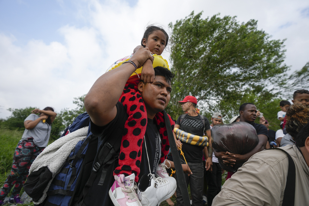 Migrant holding young girl on his shoulder as he walks amongst other people