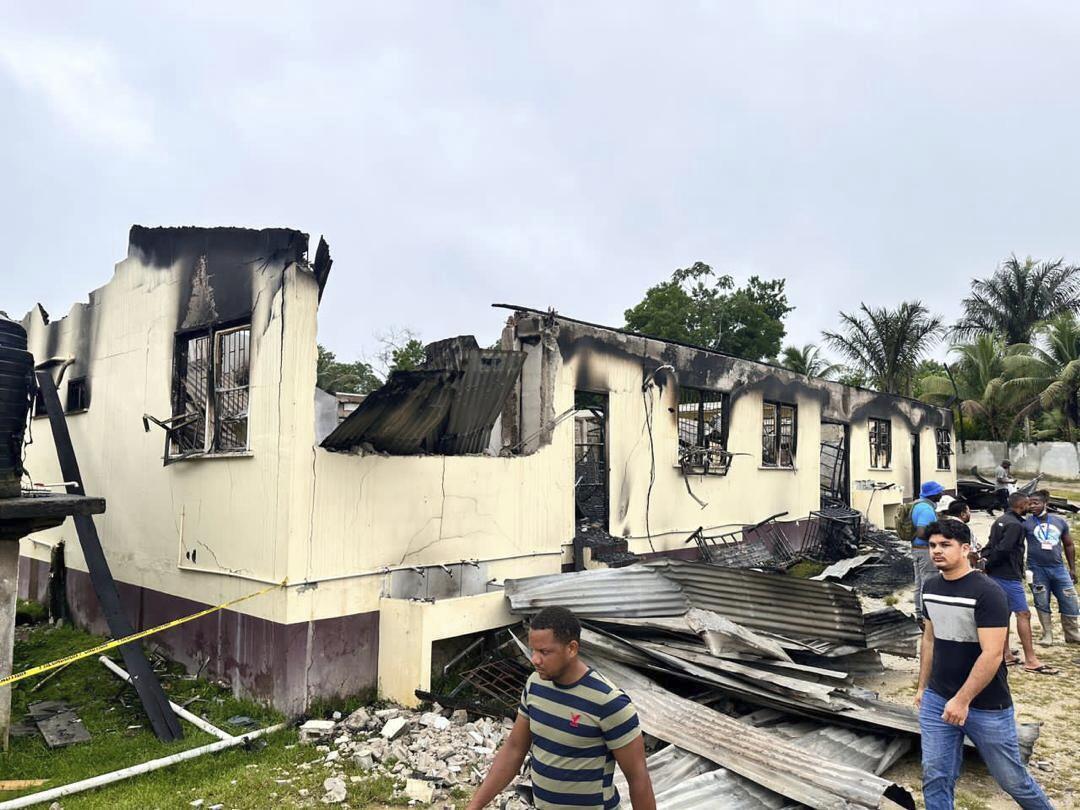 A man walks by the charred remains of a beige building without a roof and burned-out windows.