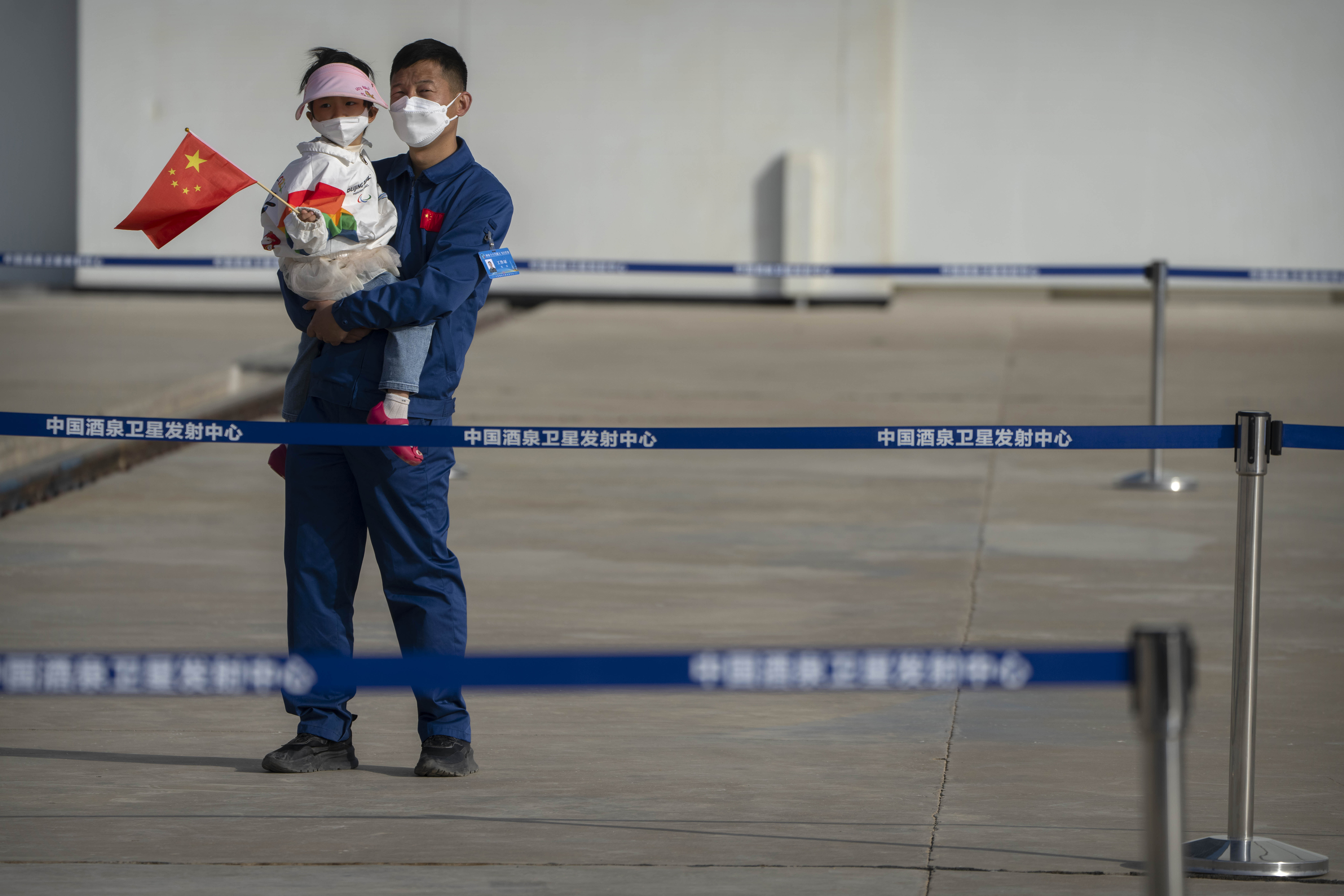 A staff member holding a child waits for the liftoff of the Shenzhou-16 spaceship