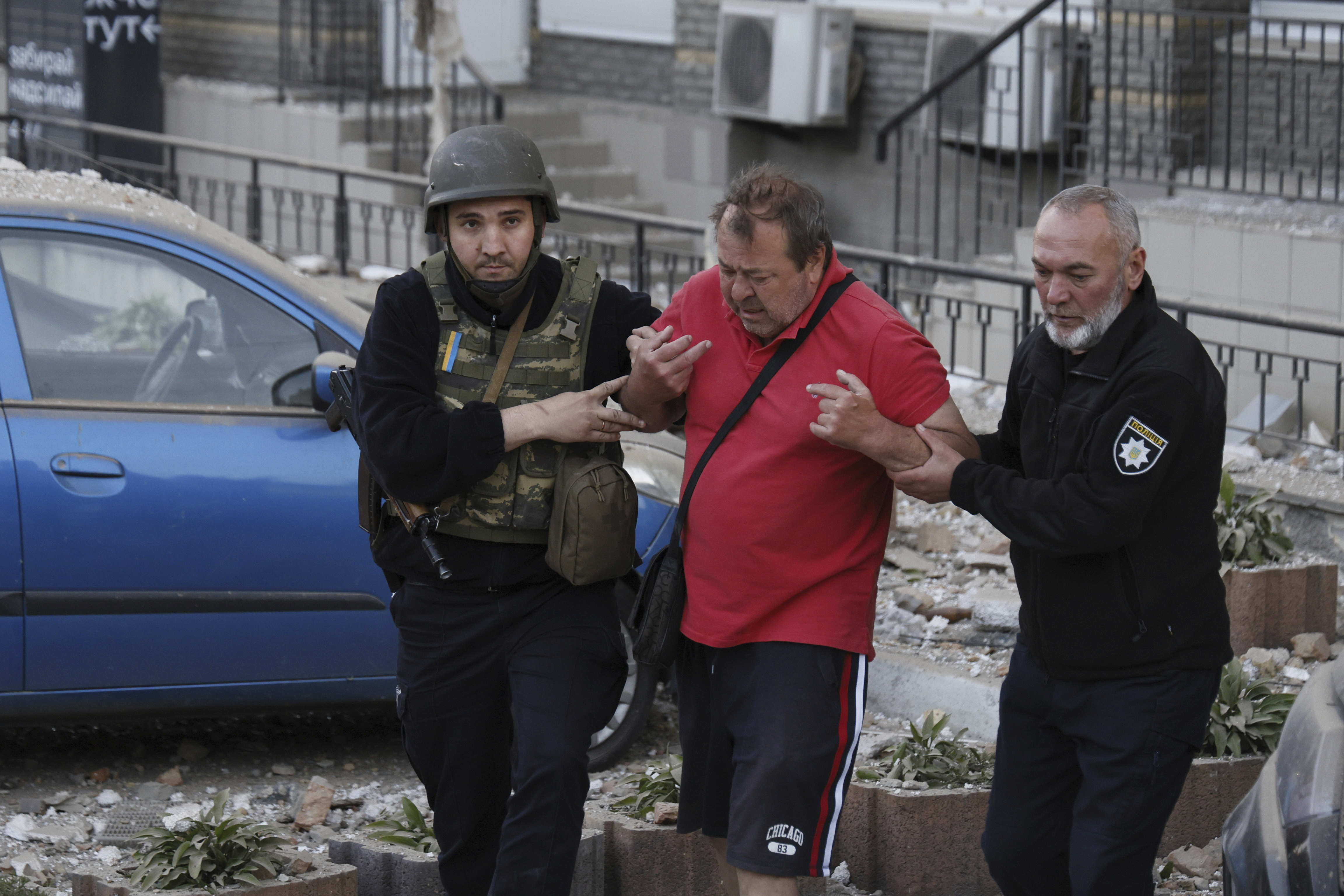 Police officers help an injured man evacuate from a multi-story apartment building to an ambulance