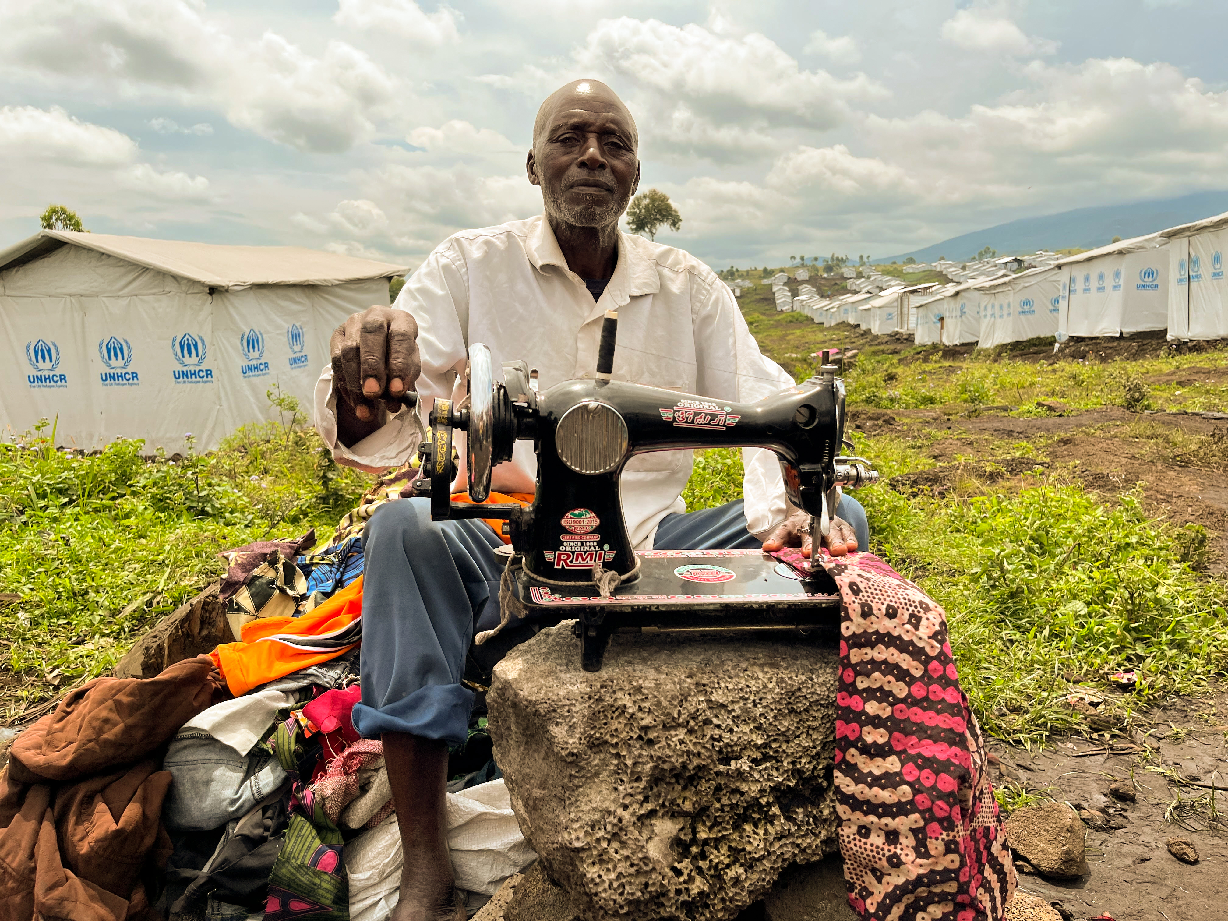 Denis Sebwage Rugemba, who was displaced by the conflict with M23, mends clothes in Bushagara Camp. [Sophie Neiman/Al Jazeera]
