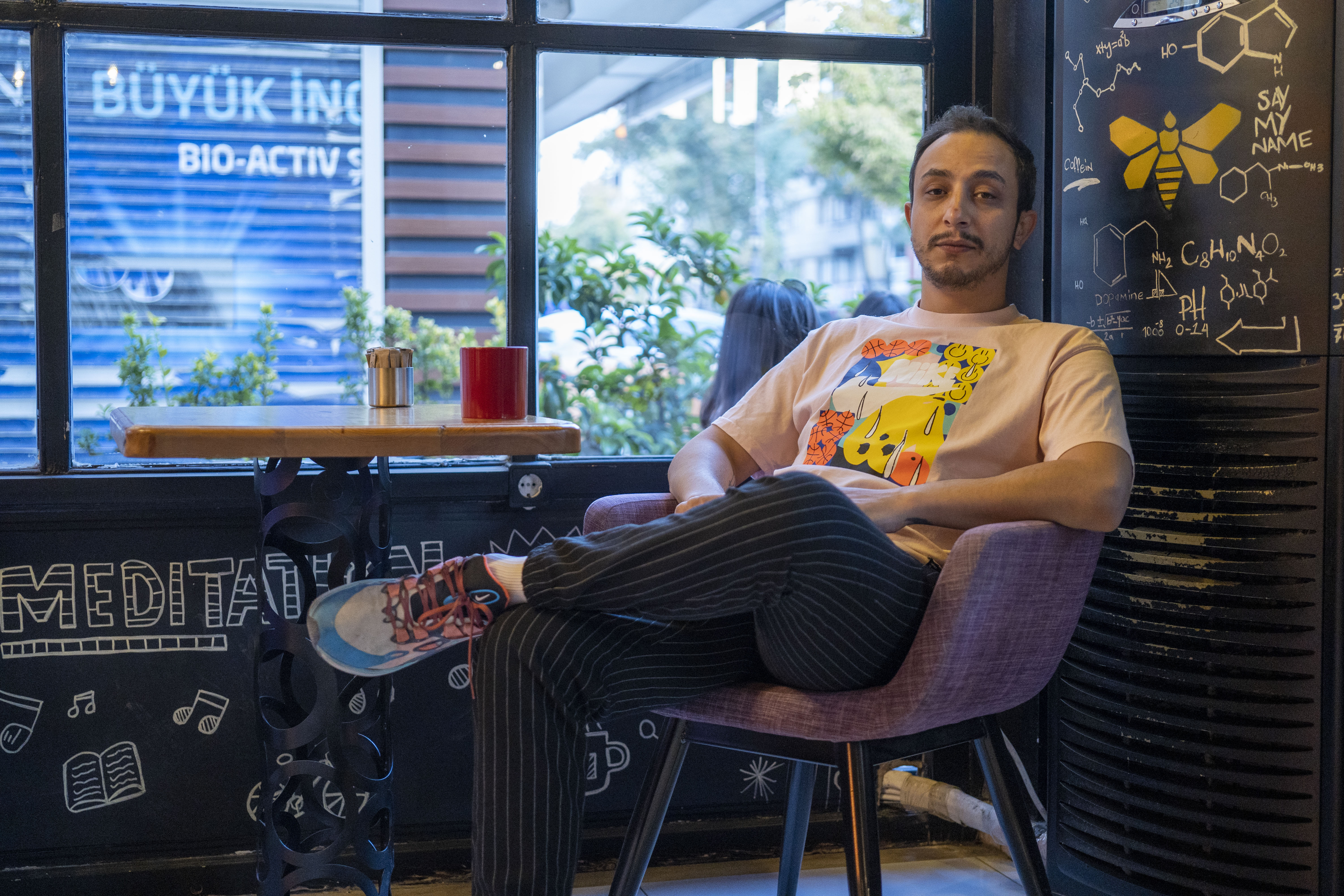 A photo of Nashwan Jamali sitting in front of a window with a blackboard behind him.