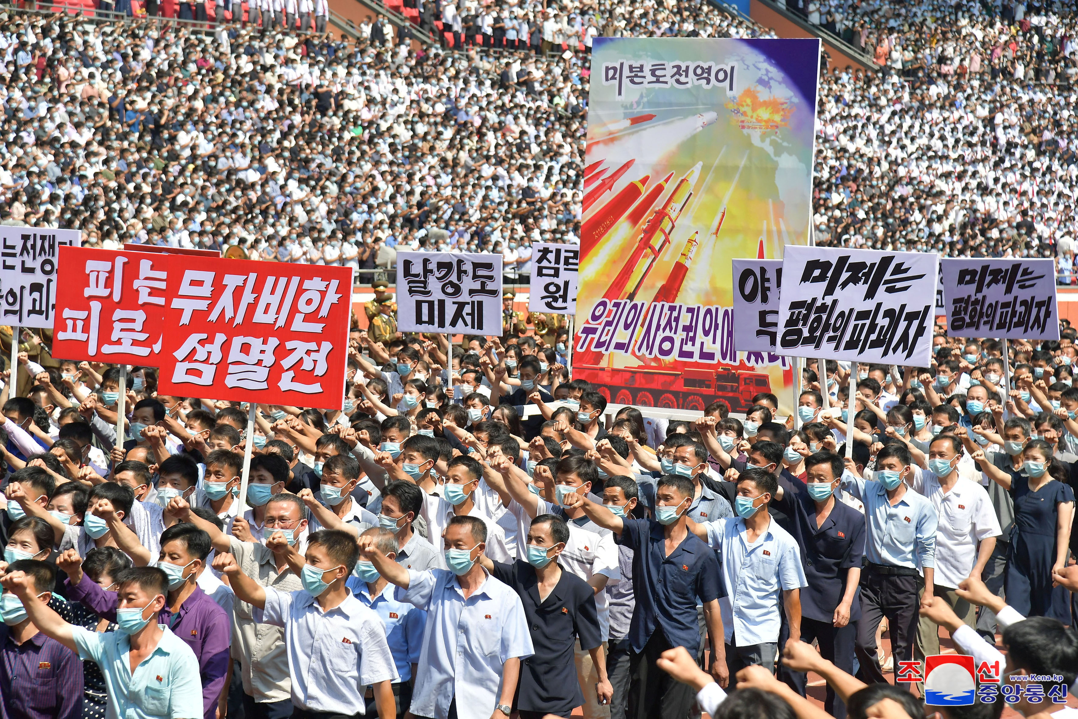 People at a mass rally in Pyongyang. They are marching and punching the air with their right hands. Thet are holding banners condemning the United States