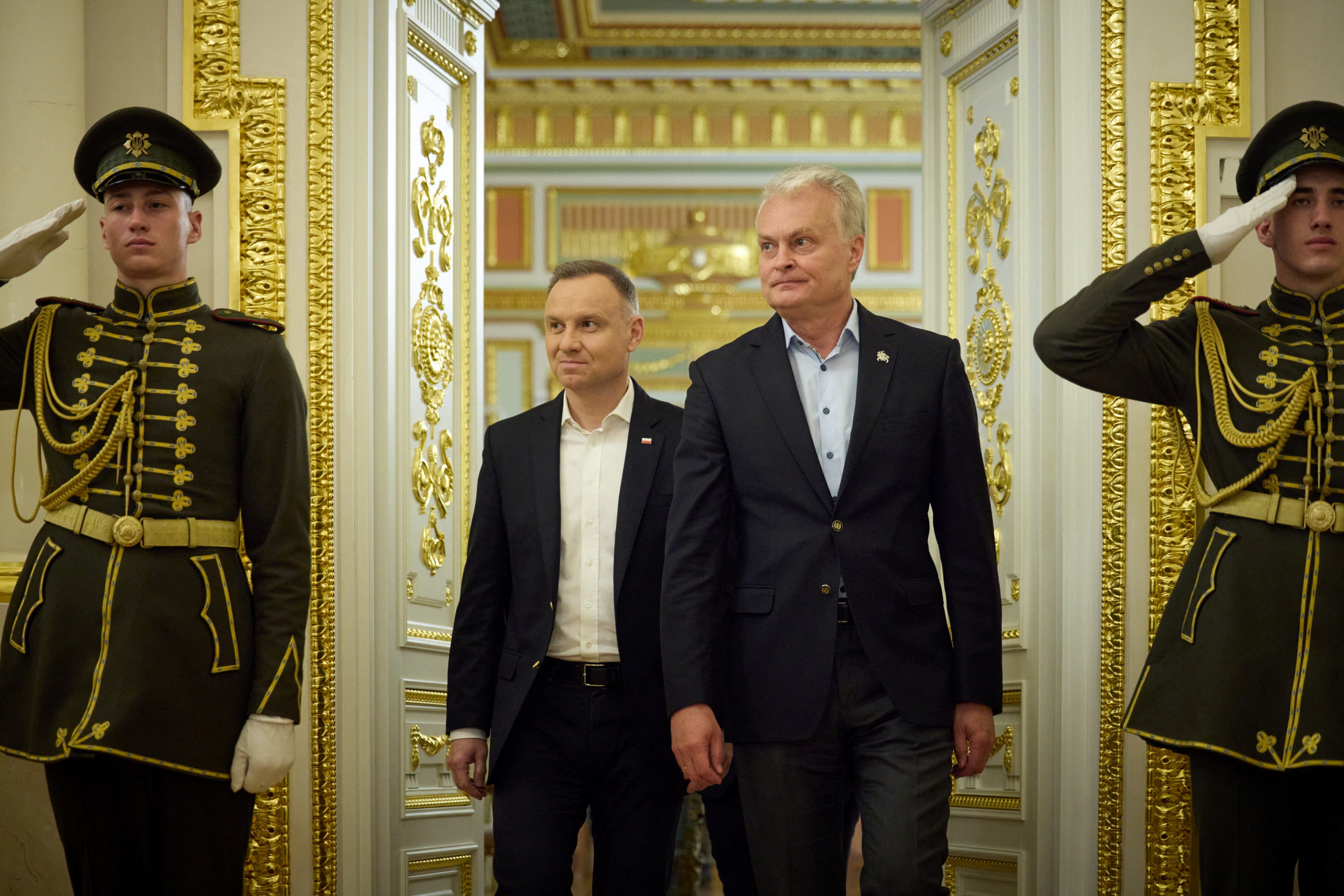 Poland's President Andrzej Duda and Lithuanian President Gitanas Nauseda arrive for a joint press conference with Ukraine's President Volodymyr Zelenskyy. The room is ornate and there are two soldiers in ceremonial dress on either side of the door.