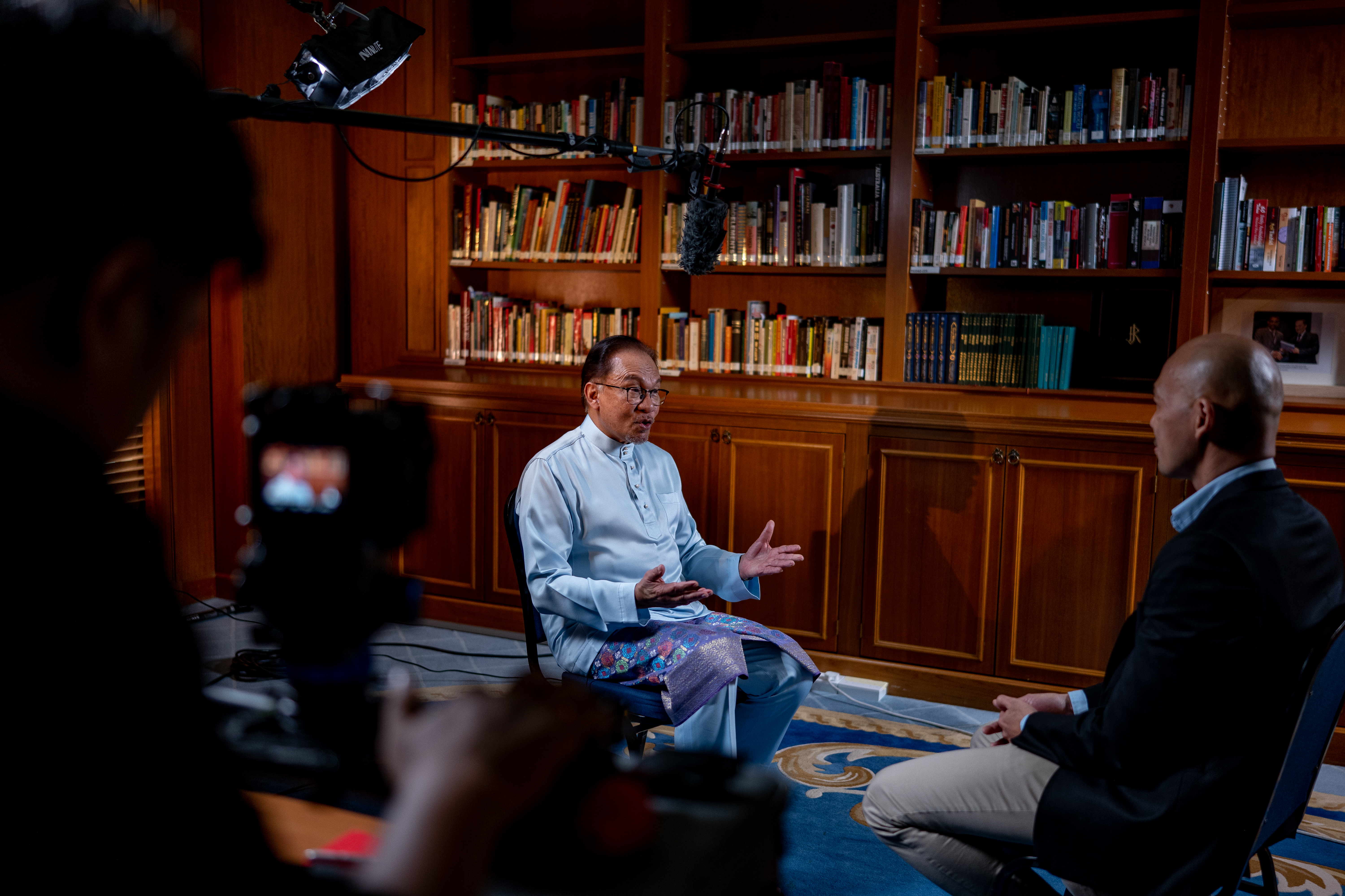 Anwar Ibrahim speaking to 101 East. He is wearing a traditional Malay outfit. His hands are spread out as he explains a point.