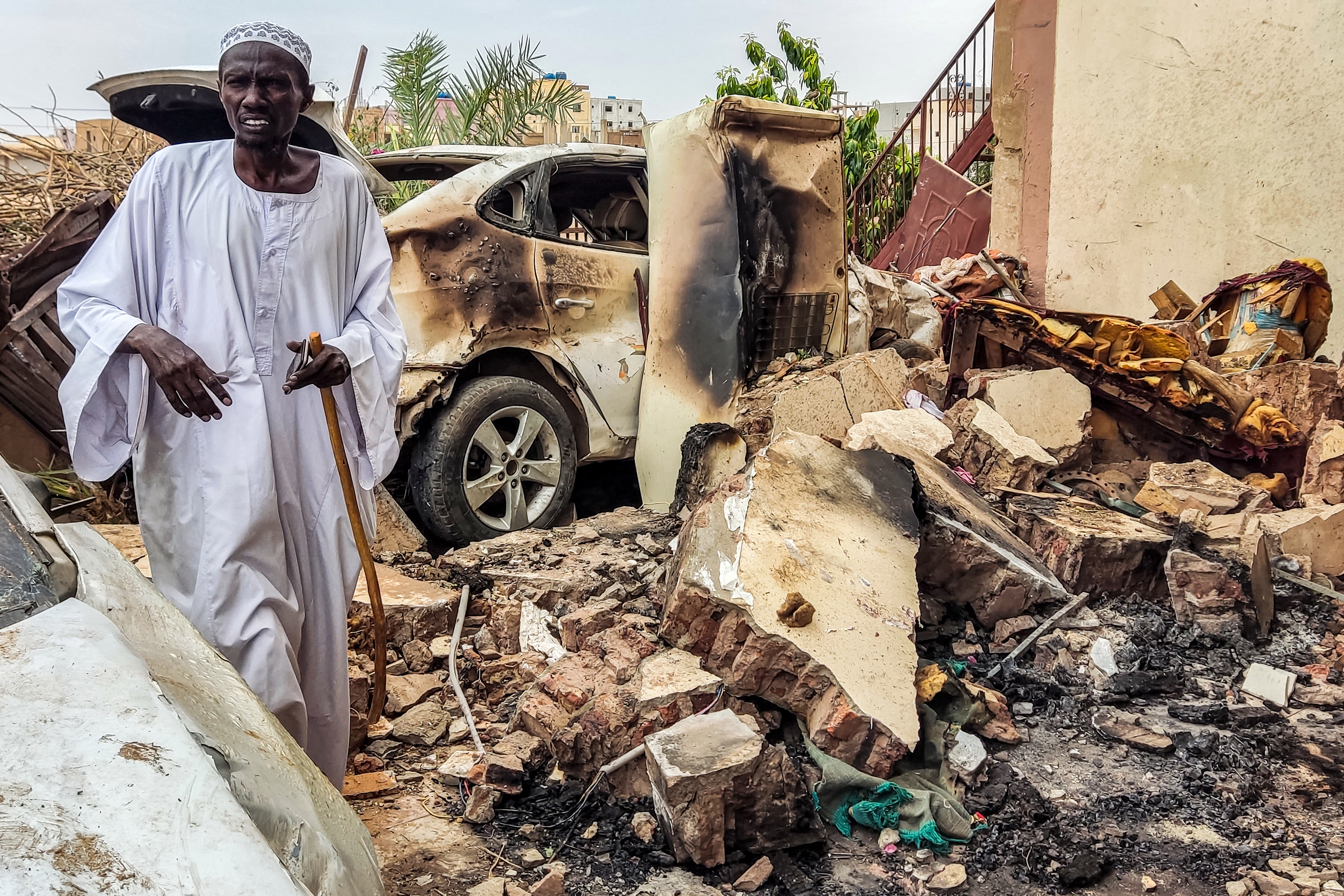 A man inspects damage as he walks through the rubble by a destroyed car outside a house