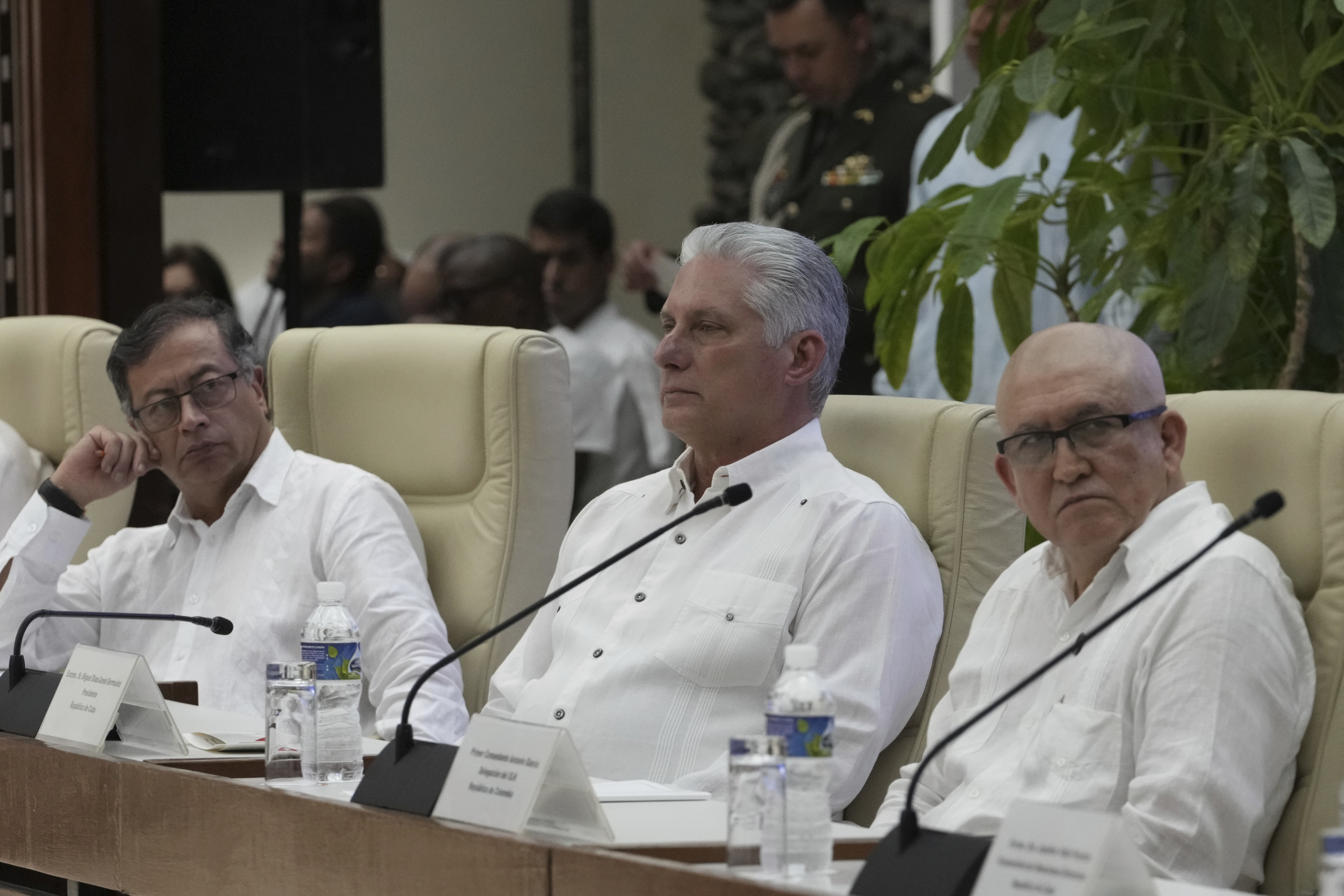Three men — all dressed in white — sit at a panel table, with microphones positioned in front of them.