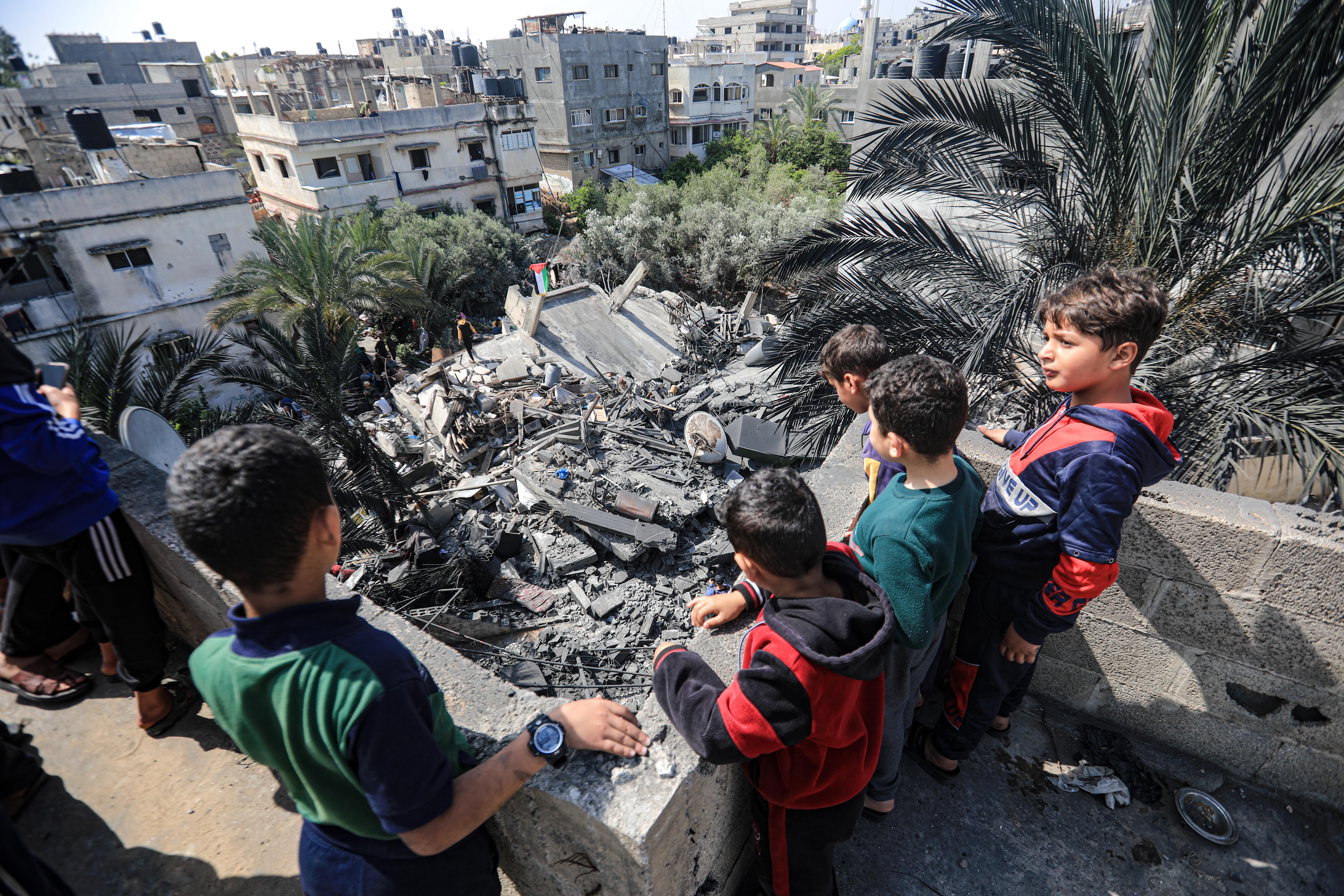 Children look on a destroyed house