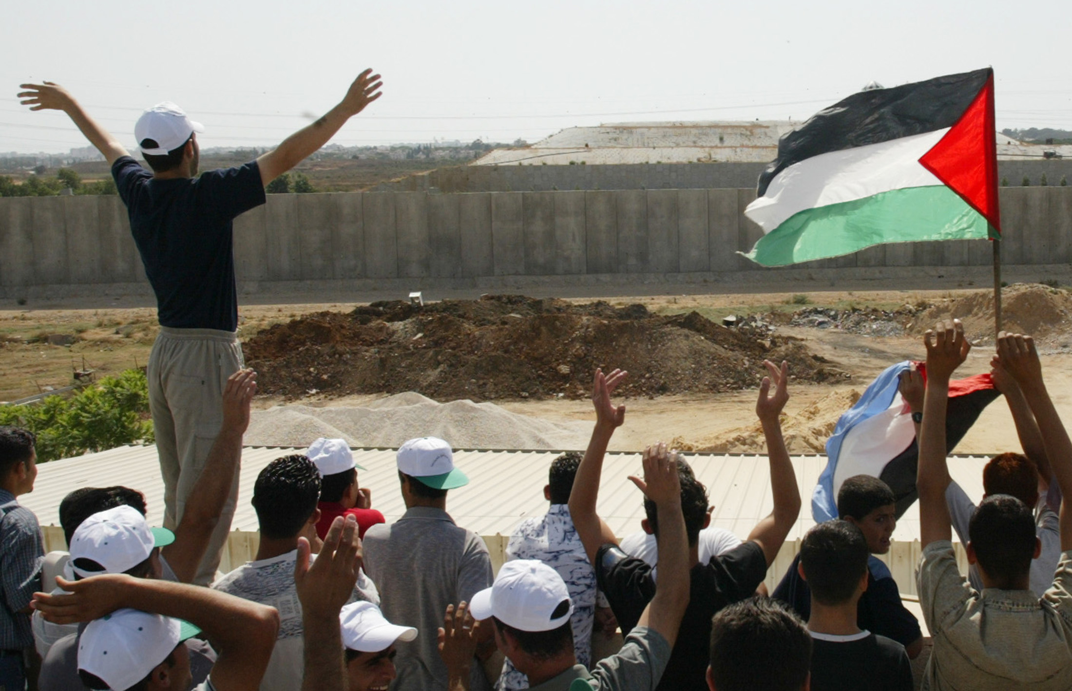 Palestinian demonstrators wave towards Israeli activist on the other side of the Israeli security wall during a rally against the separation barrier, seen in the background, that took place on both sides of the barrier near the West Bank town of Qalqiliya July 16, 2004.