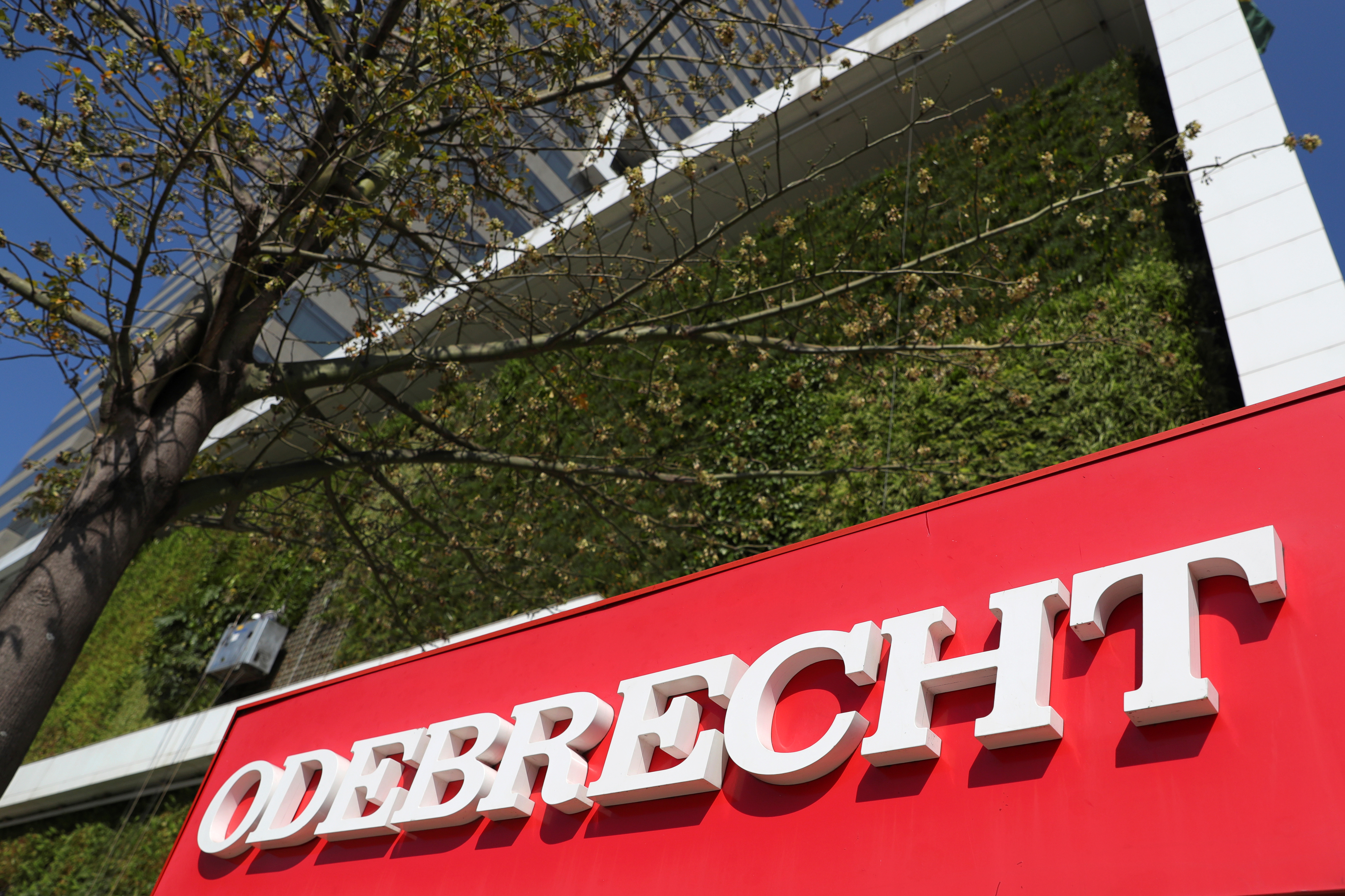 The exterior of a building shows the logo "Odebrecht." A tree grows nearby.
