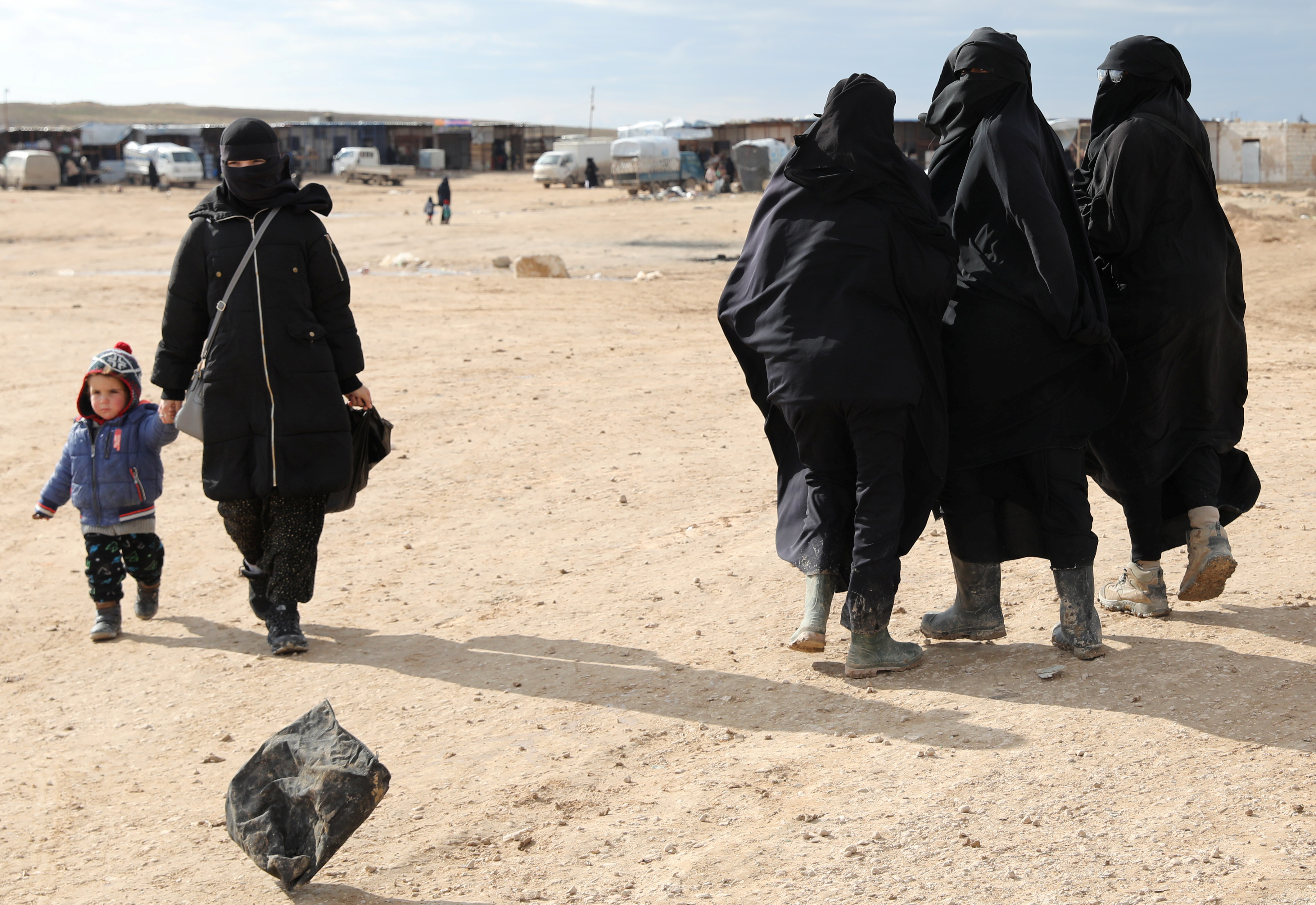 A woman holds hands with a child while walking through al-Hol camp, Syria