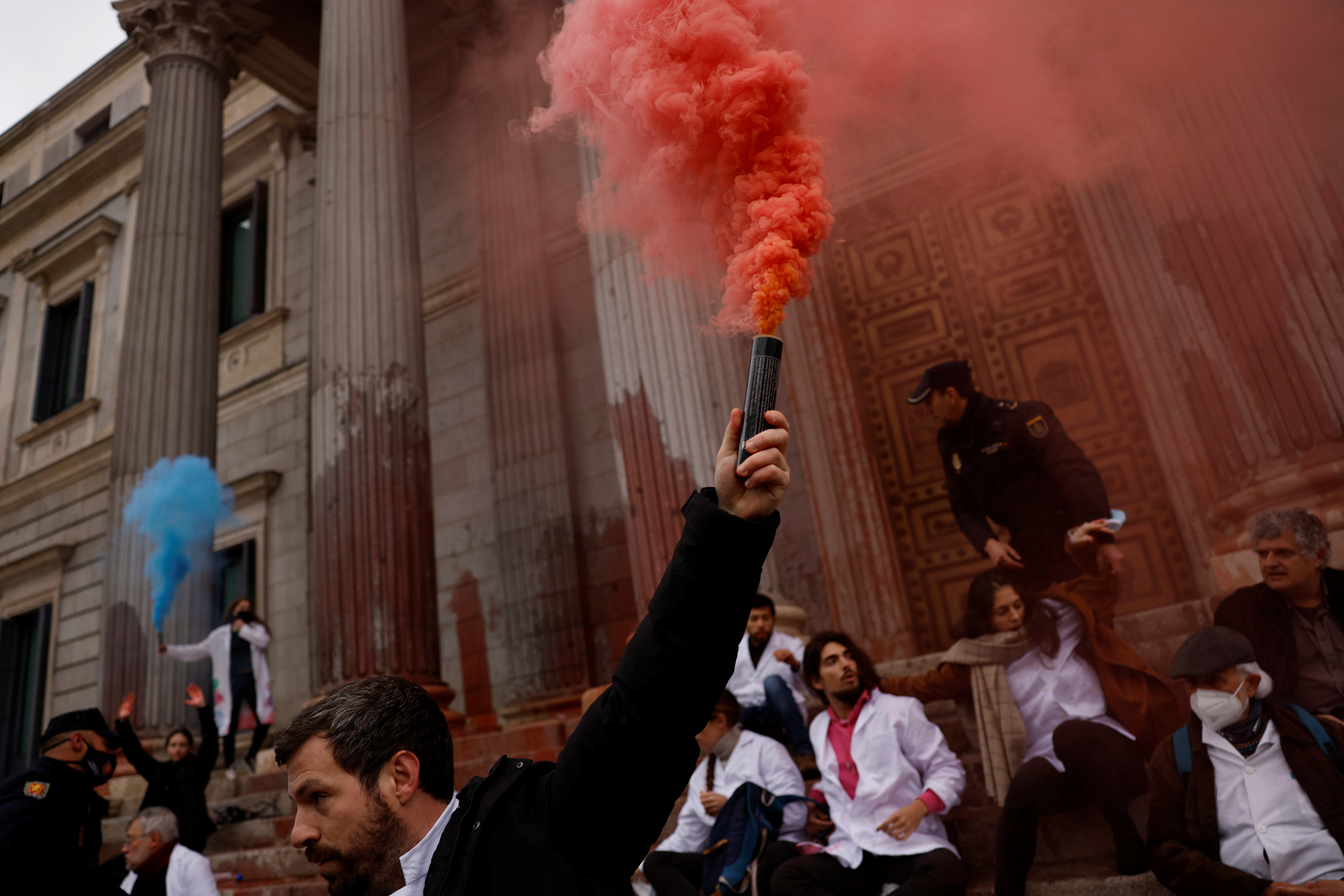 A Scientist Rebellion activist holds a smoke flare, after activists threw red paint at the exterior of the Spanish Parliament to protest climate change, in Madrid, Spain.