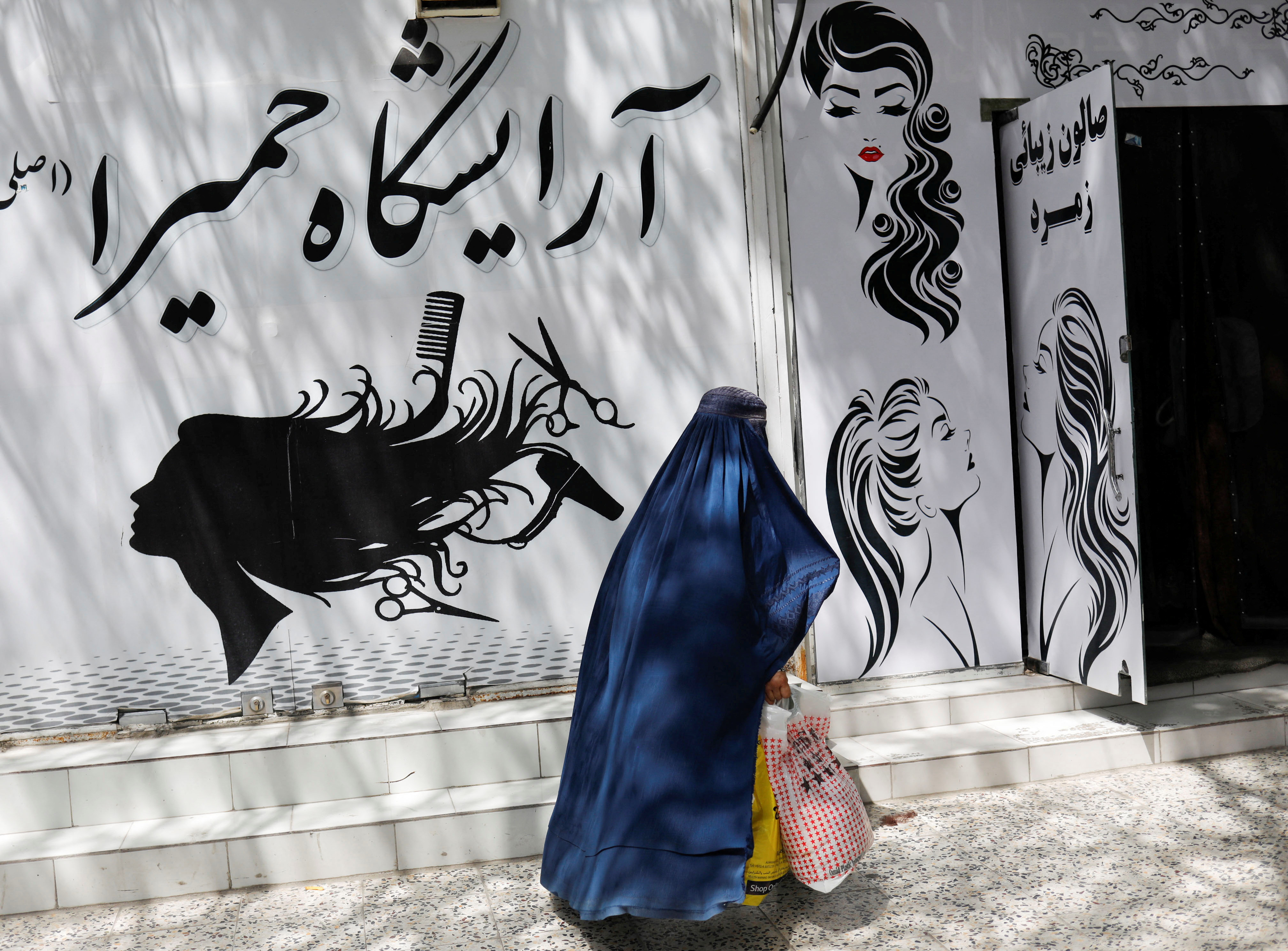 An Afghan woman walks past a beauty salon in Kabul, Afghanistan, July 6, 2023