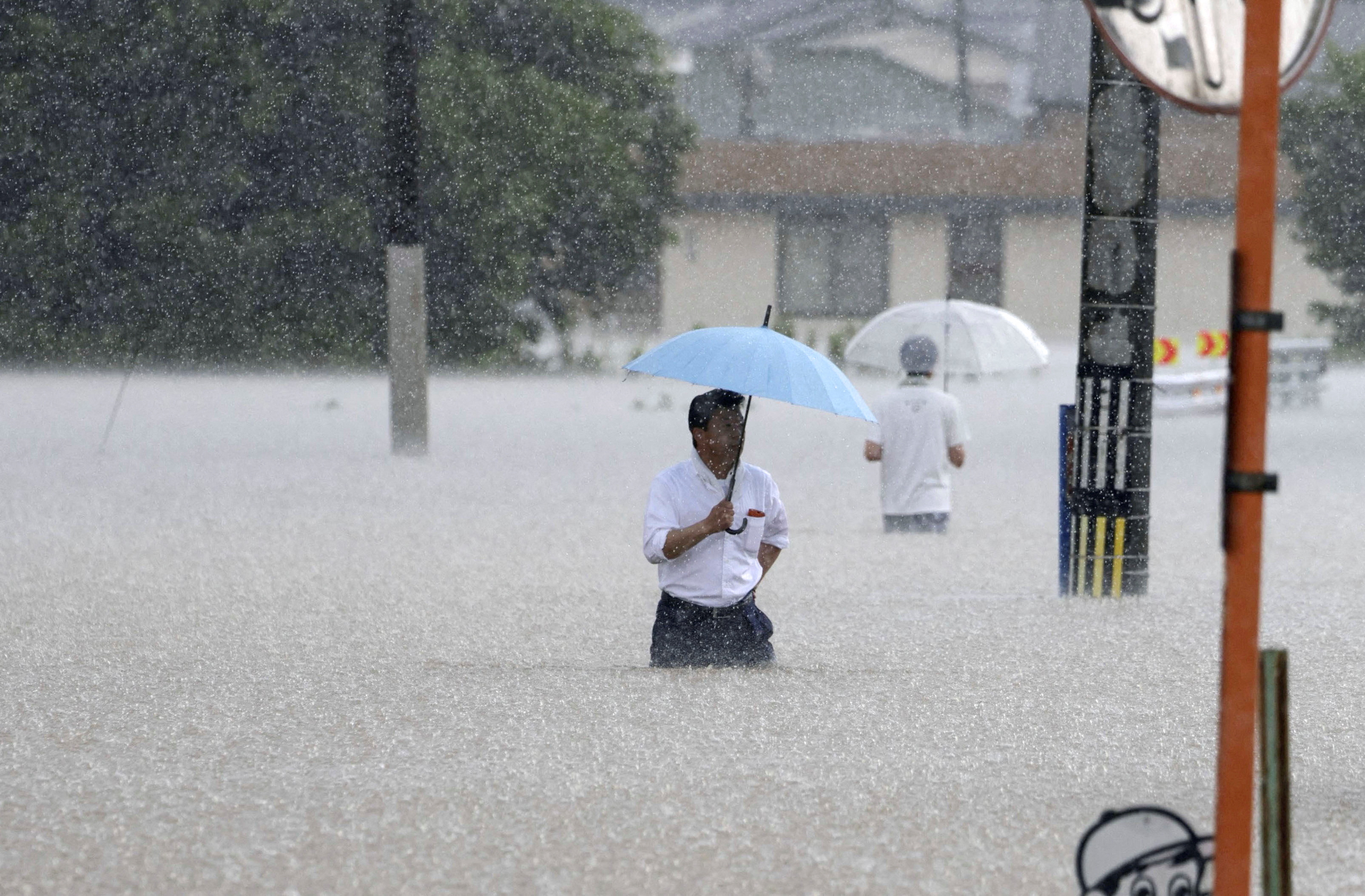 People make their way on a flooded road in heavy rain in Kurume