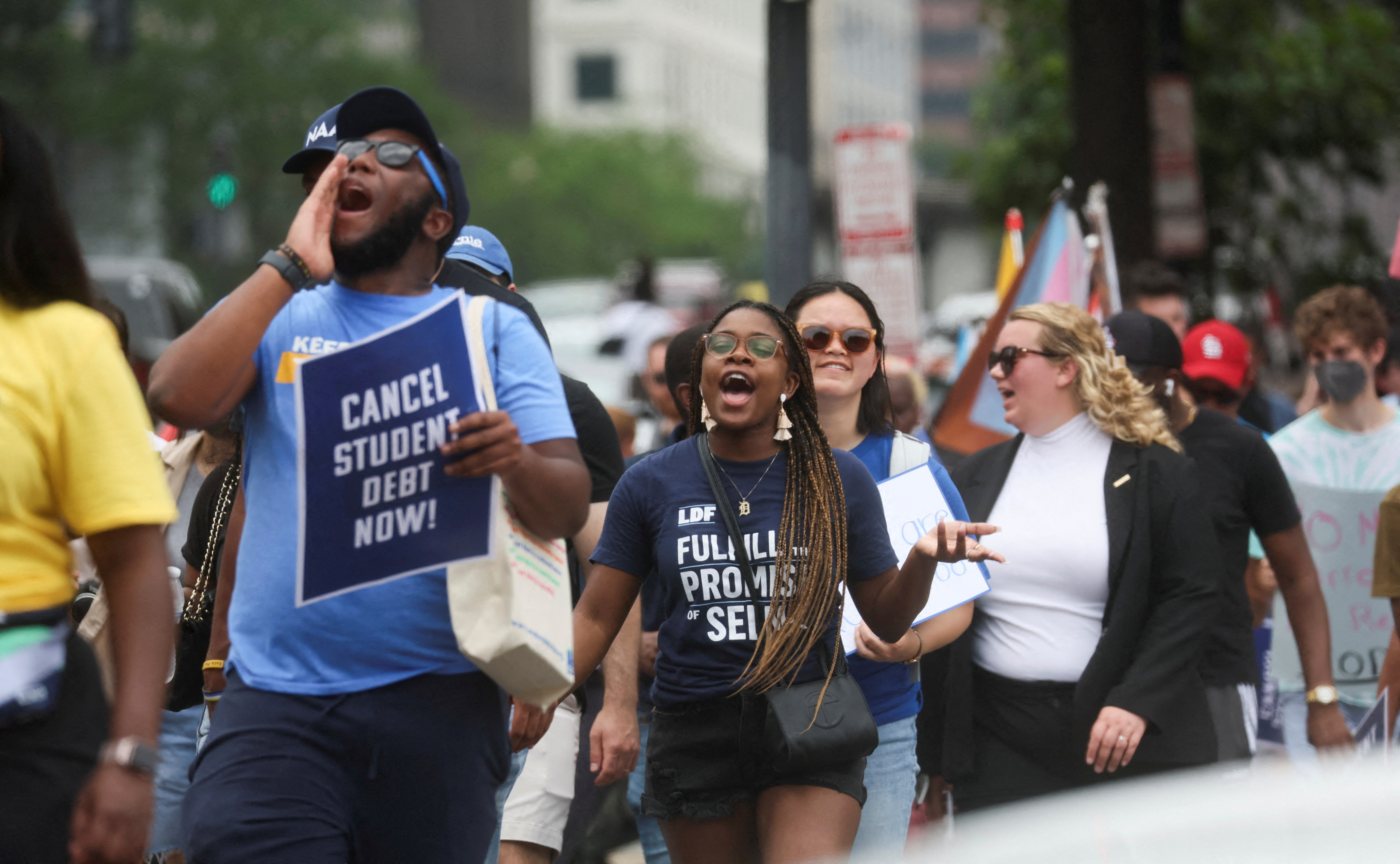 People march outside, near the White House, cupping their hands to their mouths as they chant and holding signs that read: "Cancel student debt now!"