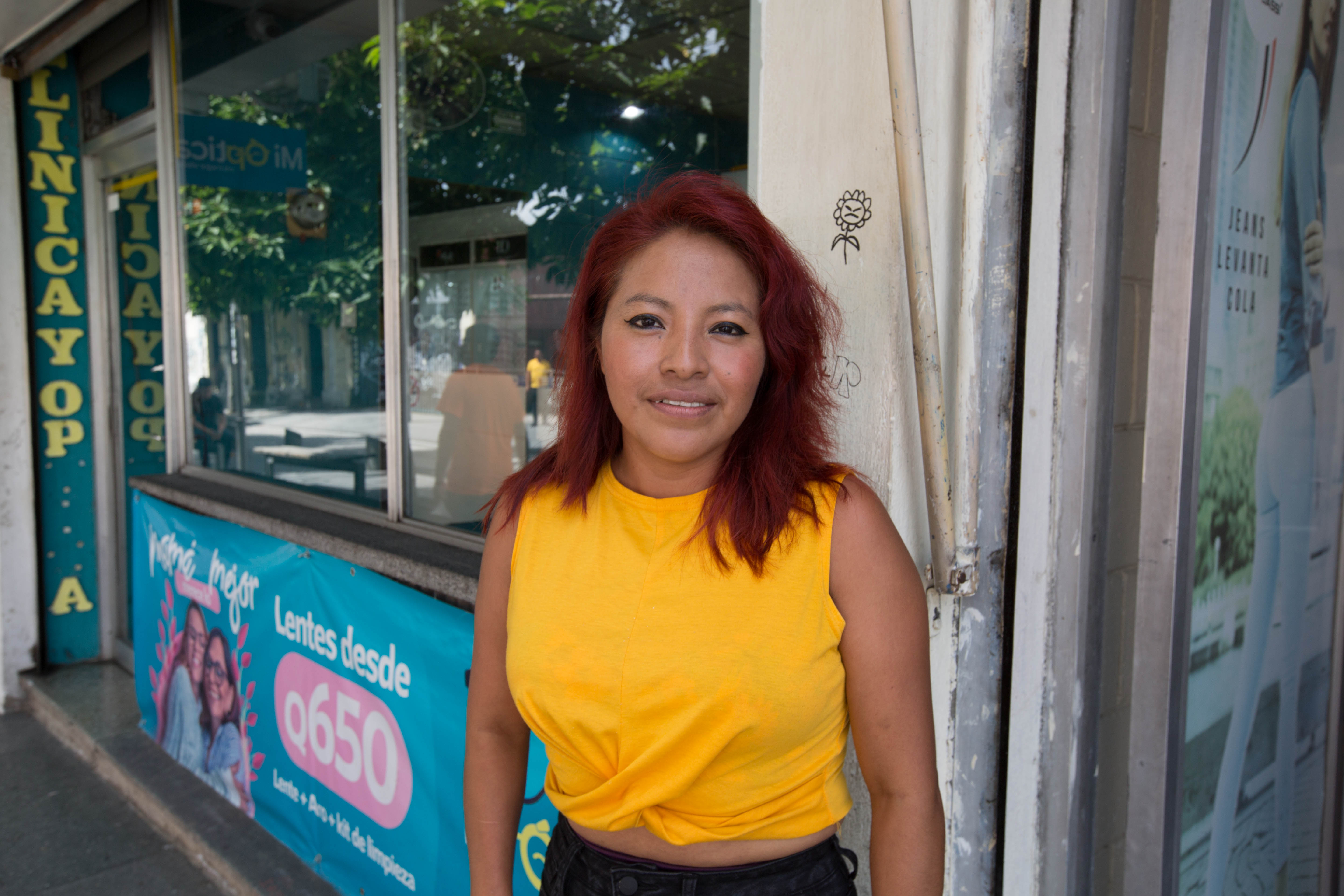A woman in a yellow sleeveless T-shirt stands outside a shop in Guatemala City.