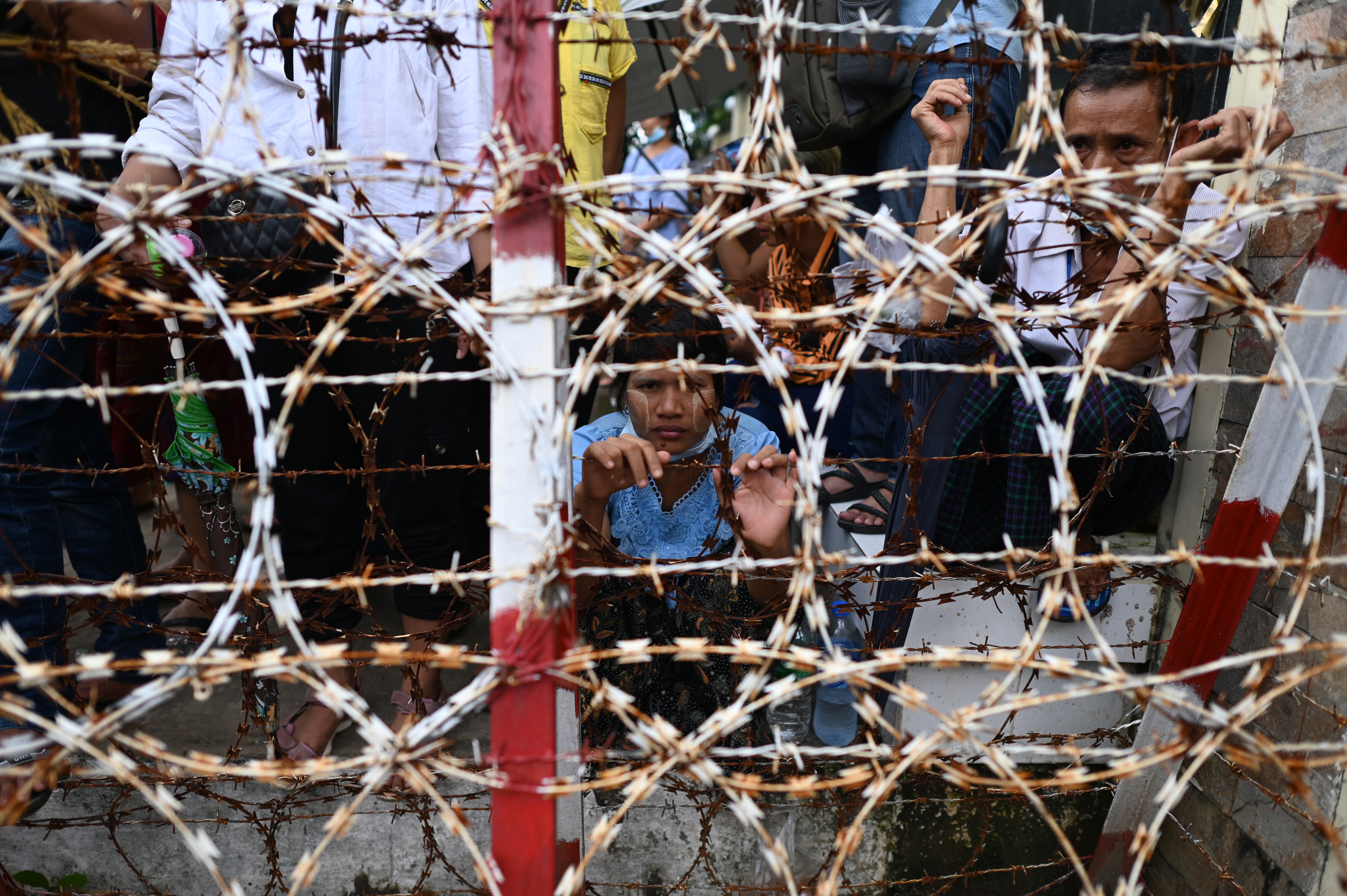 a woman looking out between gaps in razor wire as she waits in a crowd outside Yangon's Insein prison