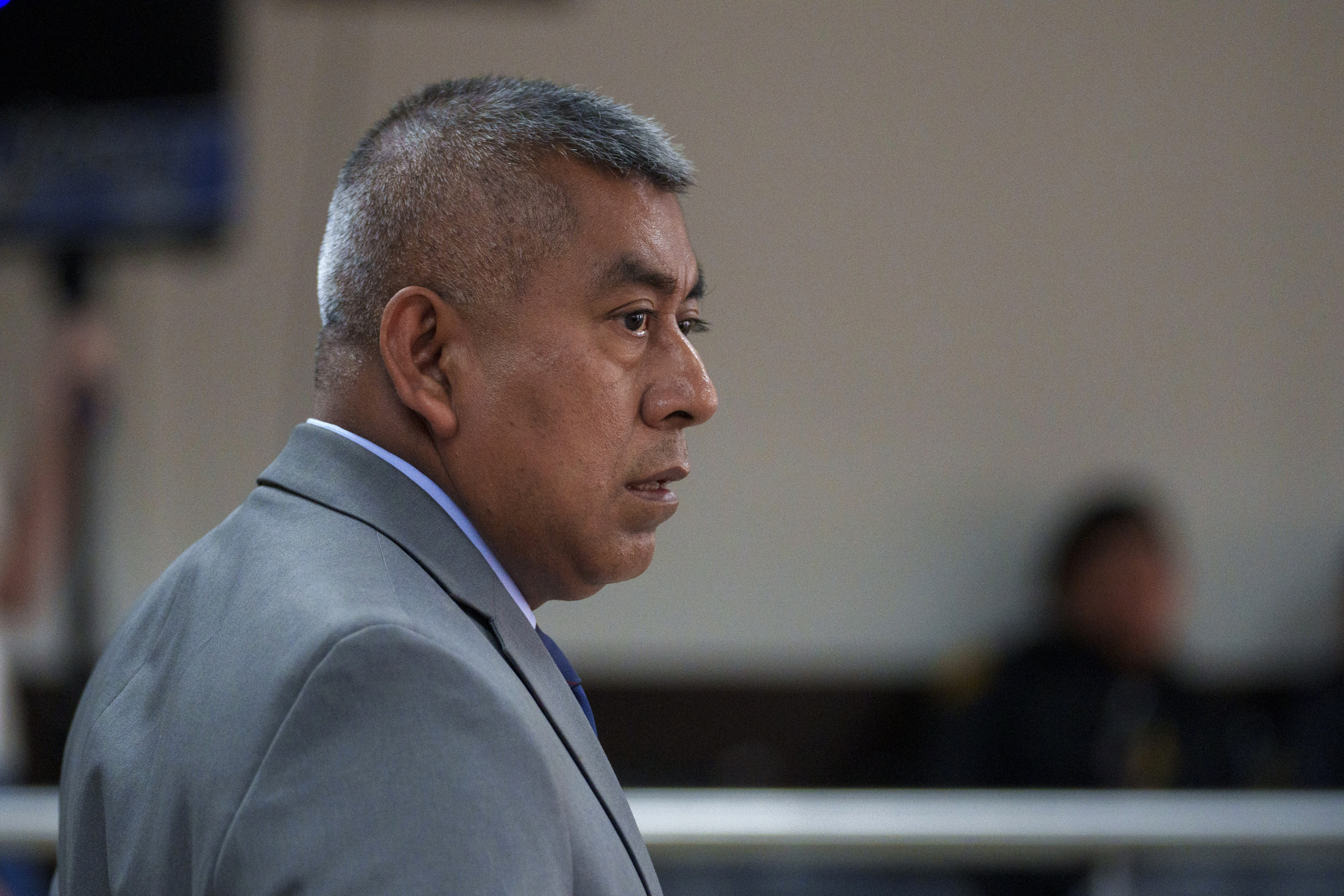 A man in a grey suit stands in a courtroom.