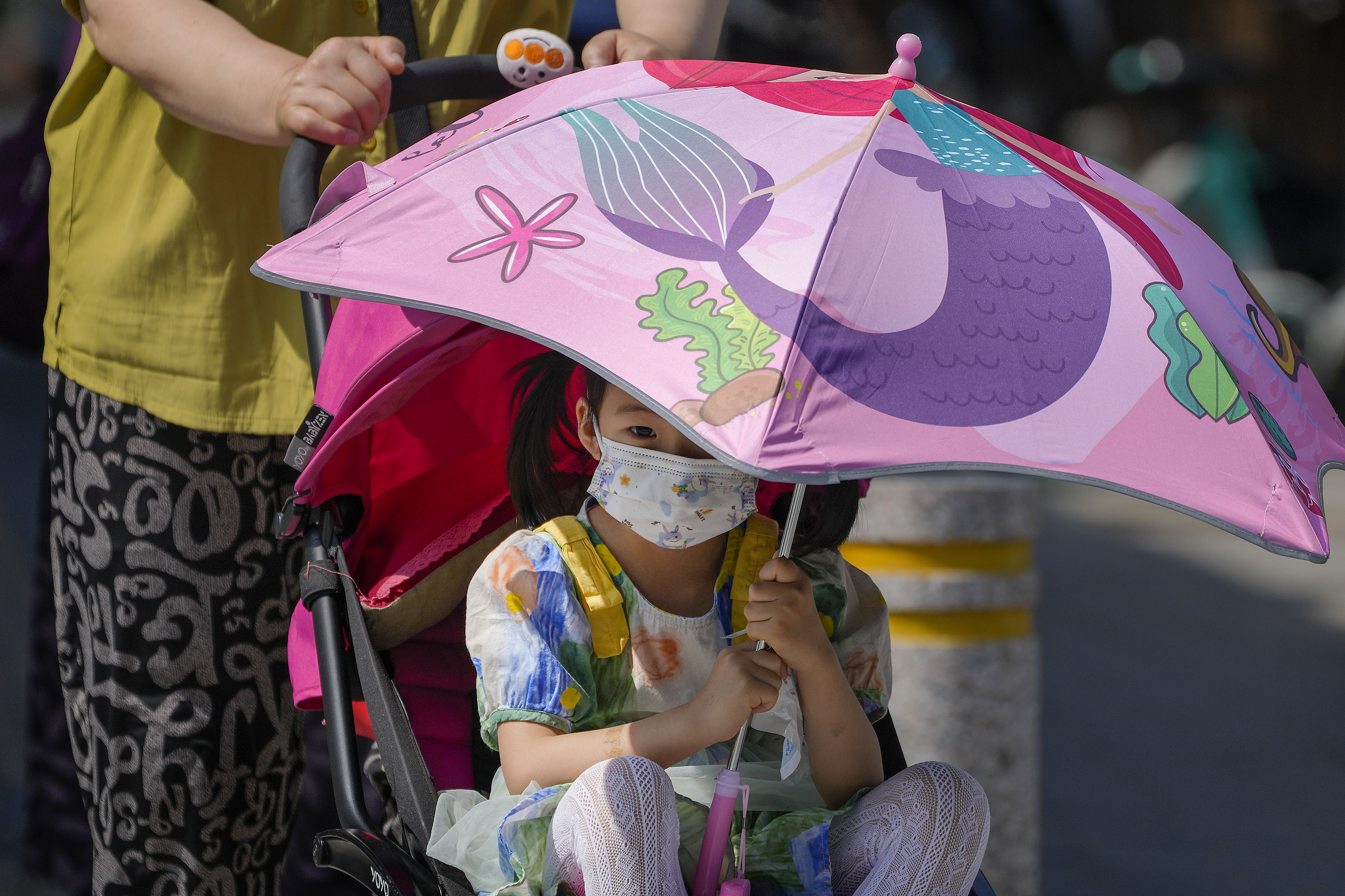 A child sits on a stroller holding an umbrella to shield from the sun as the capital city was hit by heatwave in Beijing, Monday, June 5, 2023. (AP Photo/Andy Wong)