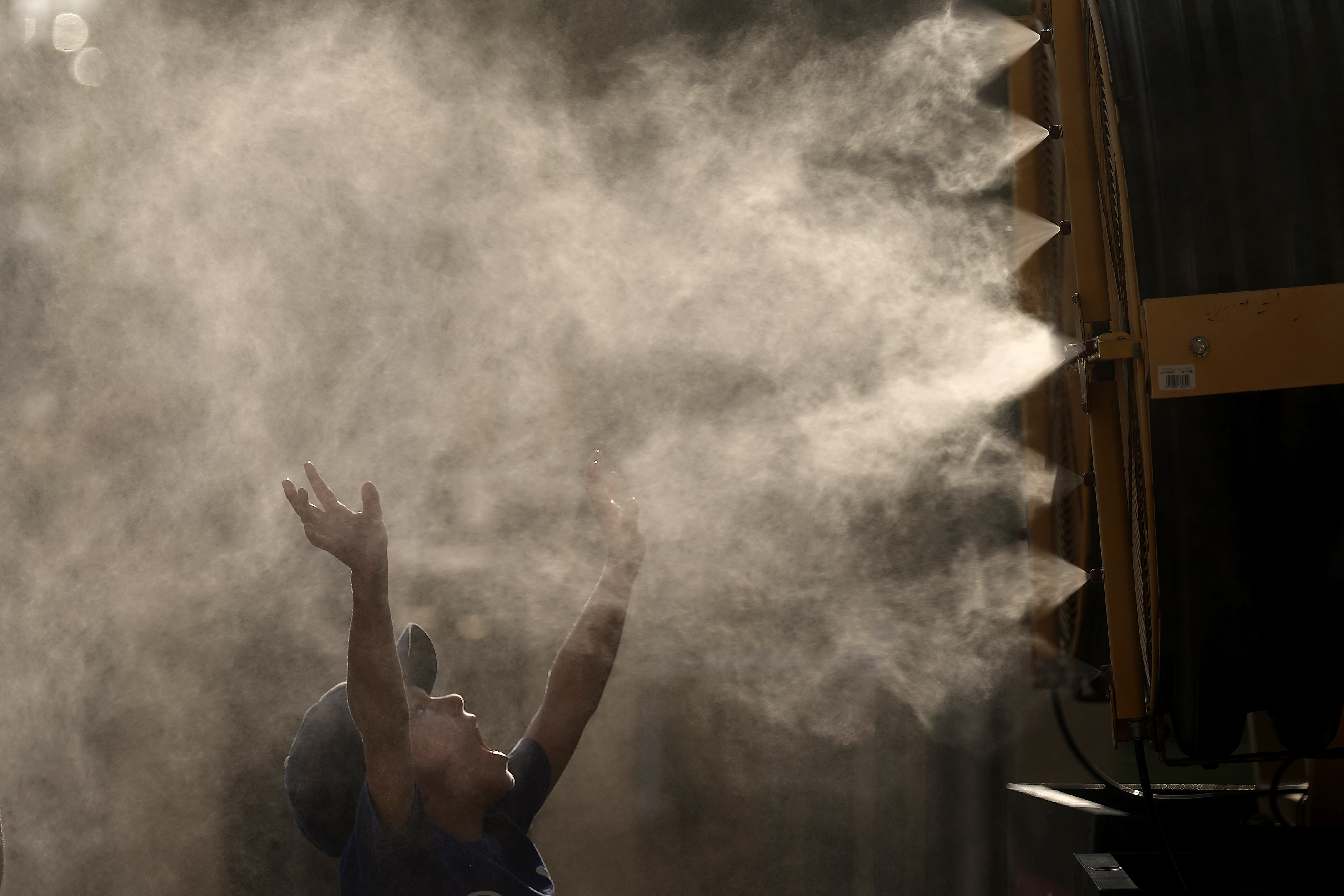 Lucas Harrington, age 7, cools off in a mister at Kauffman Stadium as temperatures approach 100 degrees fahrenheit before a baseball game between the Kansas City Royals