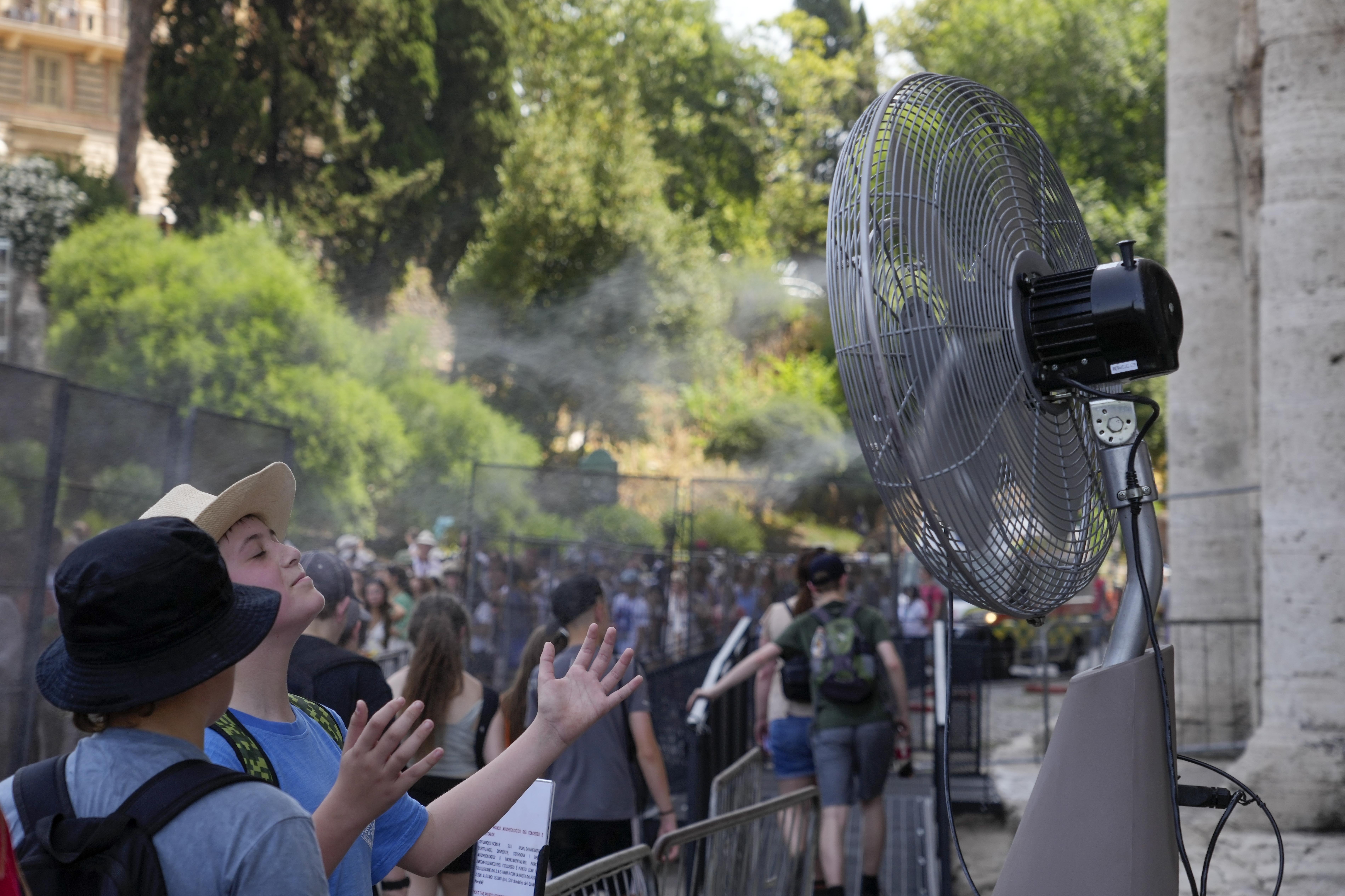 Tourists cool off near a fan as they queue to enter Rome's Colosseum,