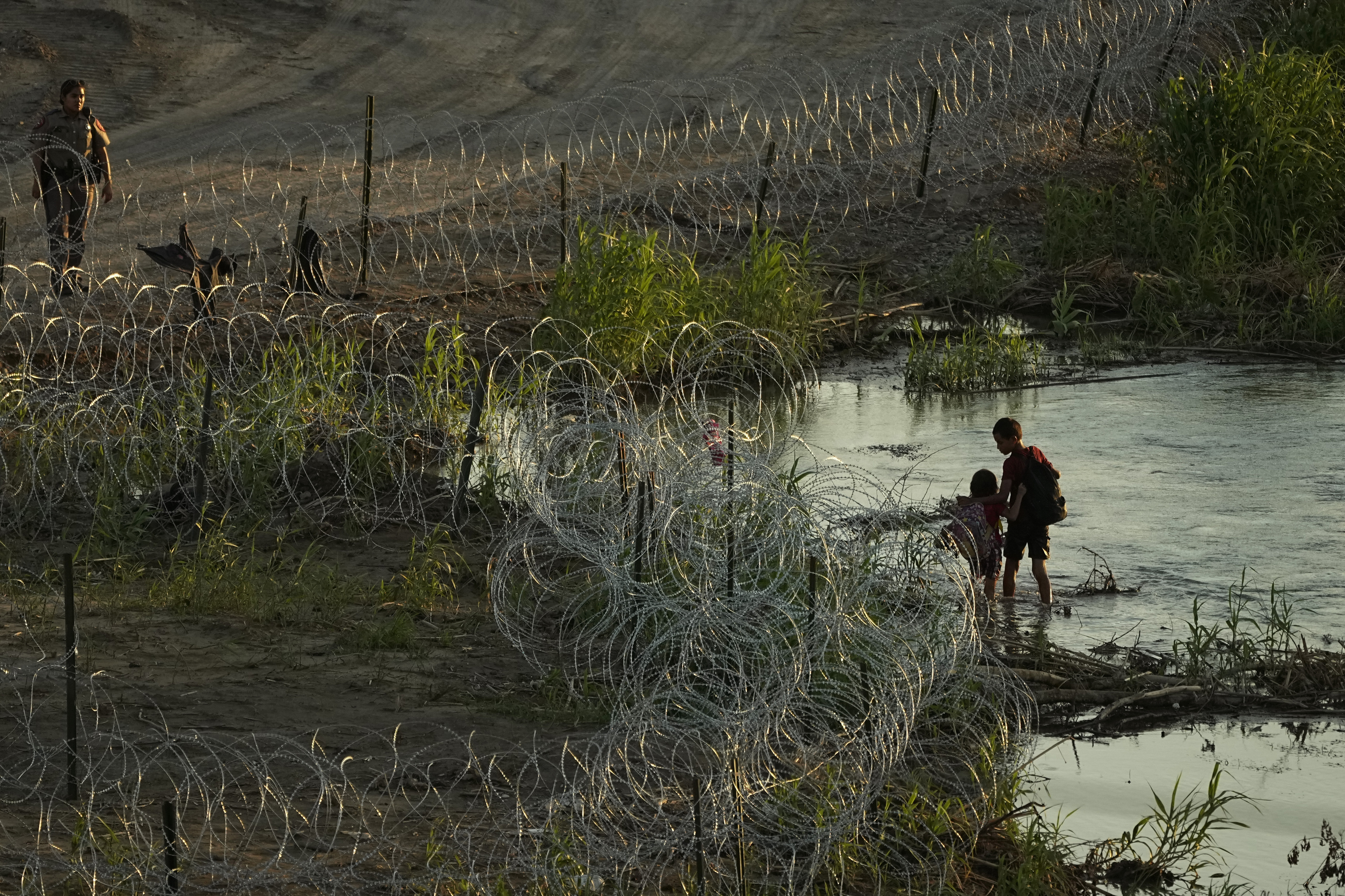 A Texas state trooper watches as young migrants walk along concertina wire