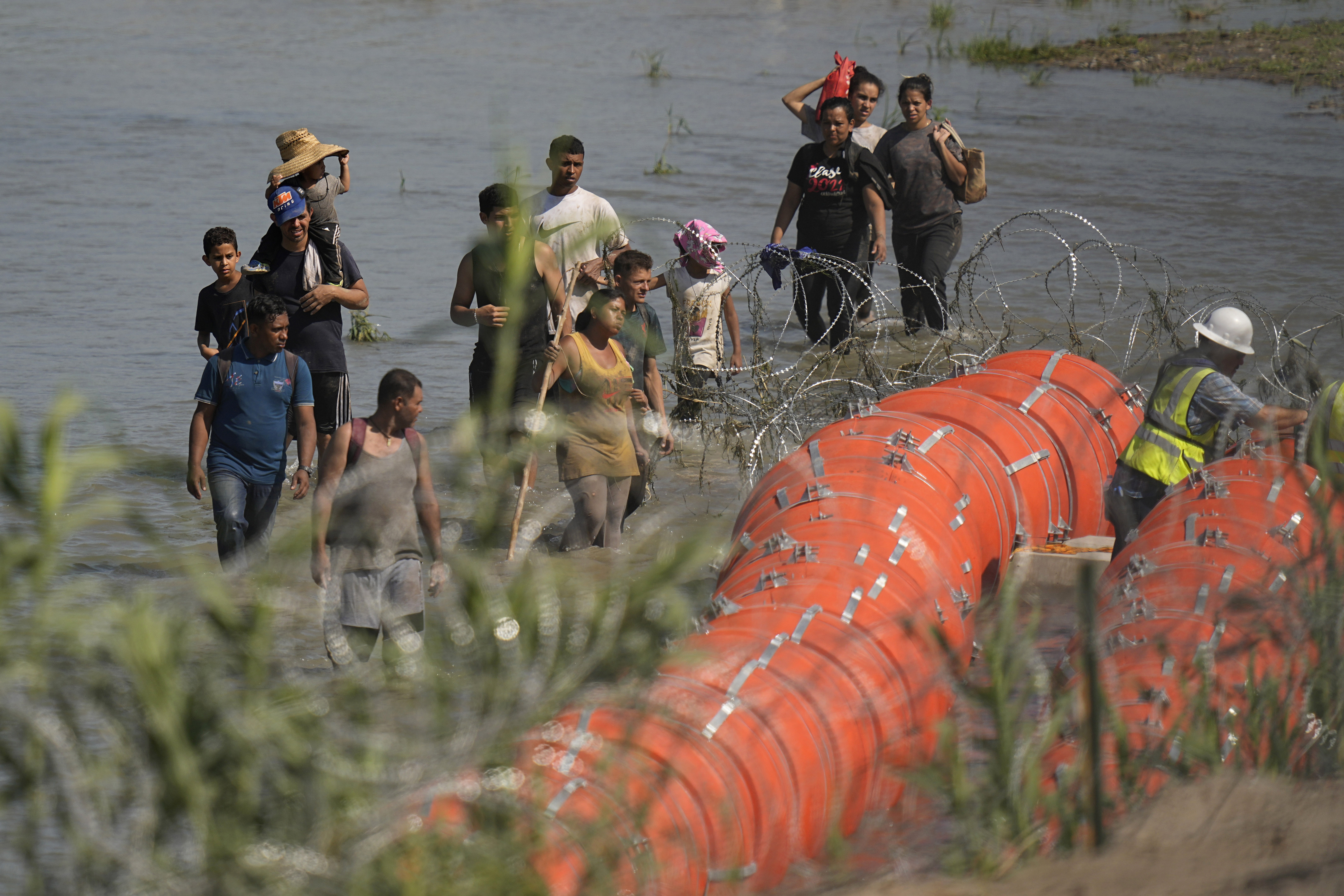 Migrants trying to enter the U.S. from Mexico approach the site where workers are assembling large buoys to be used as a border barrier