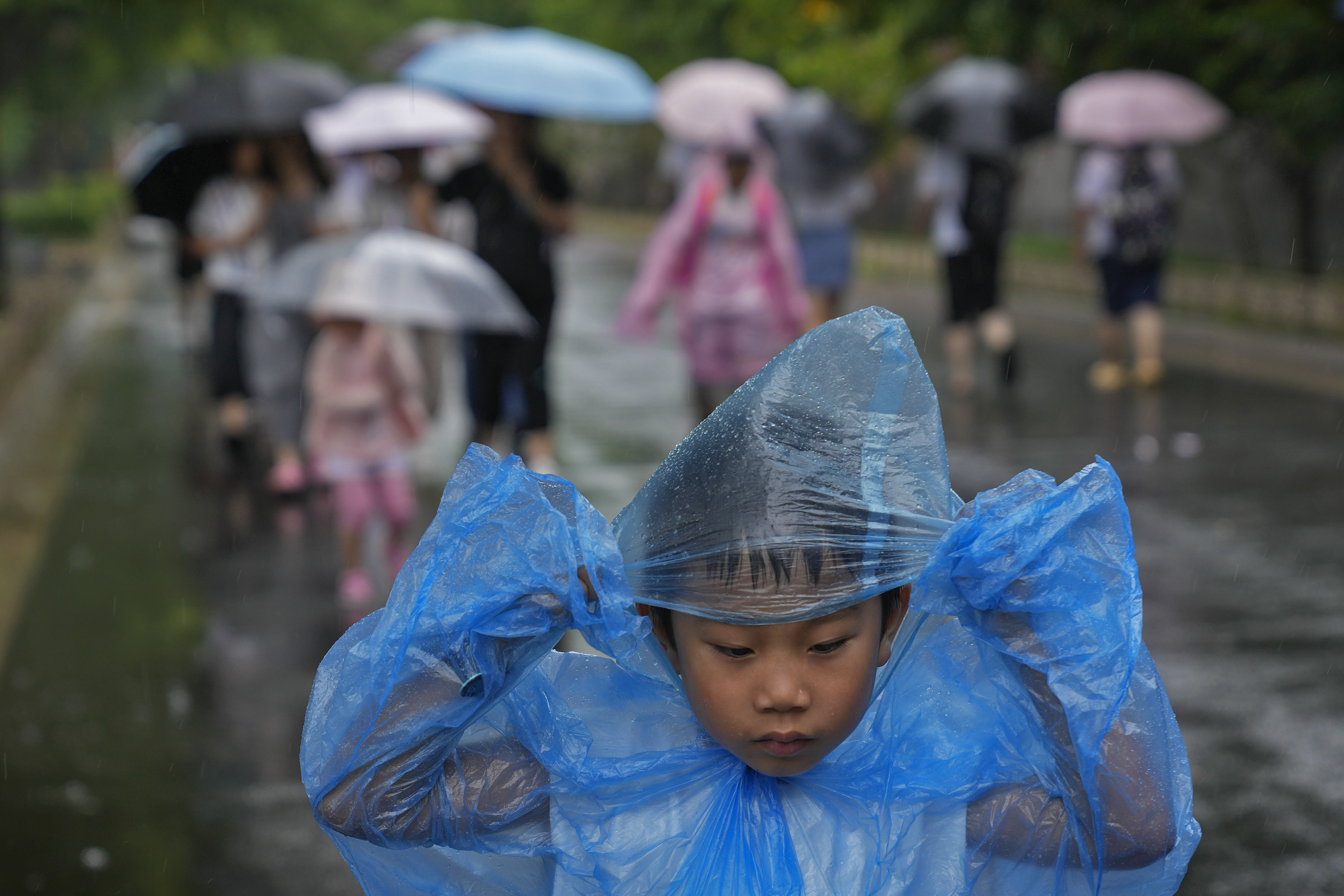 A child wearing a rain cover walks as visitors tour near the closed Forbidden City as a rainstorm soak Beijing, Sunday, July 30, 2023.