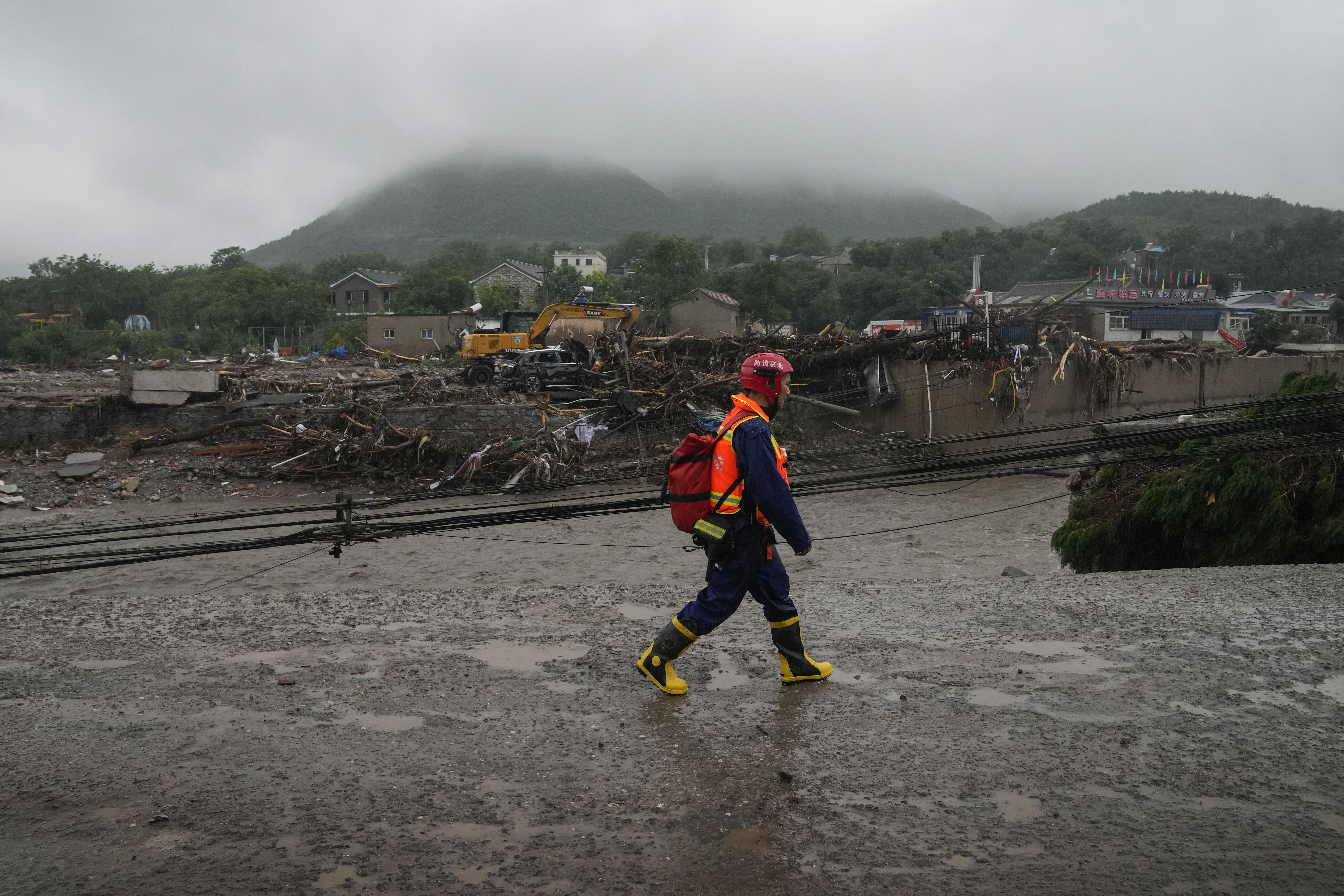 A rescue worker walks by a village near a riverbank damaged by flood water in the Mentougou District
