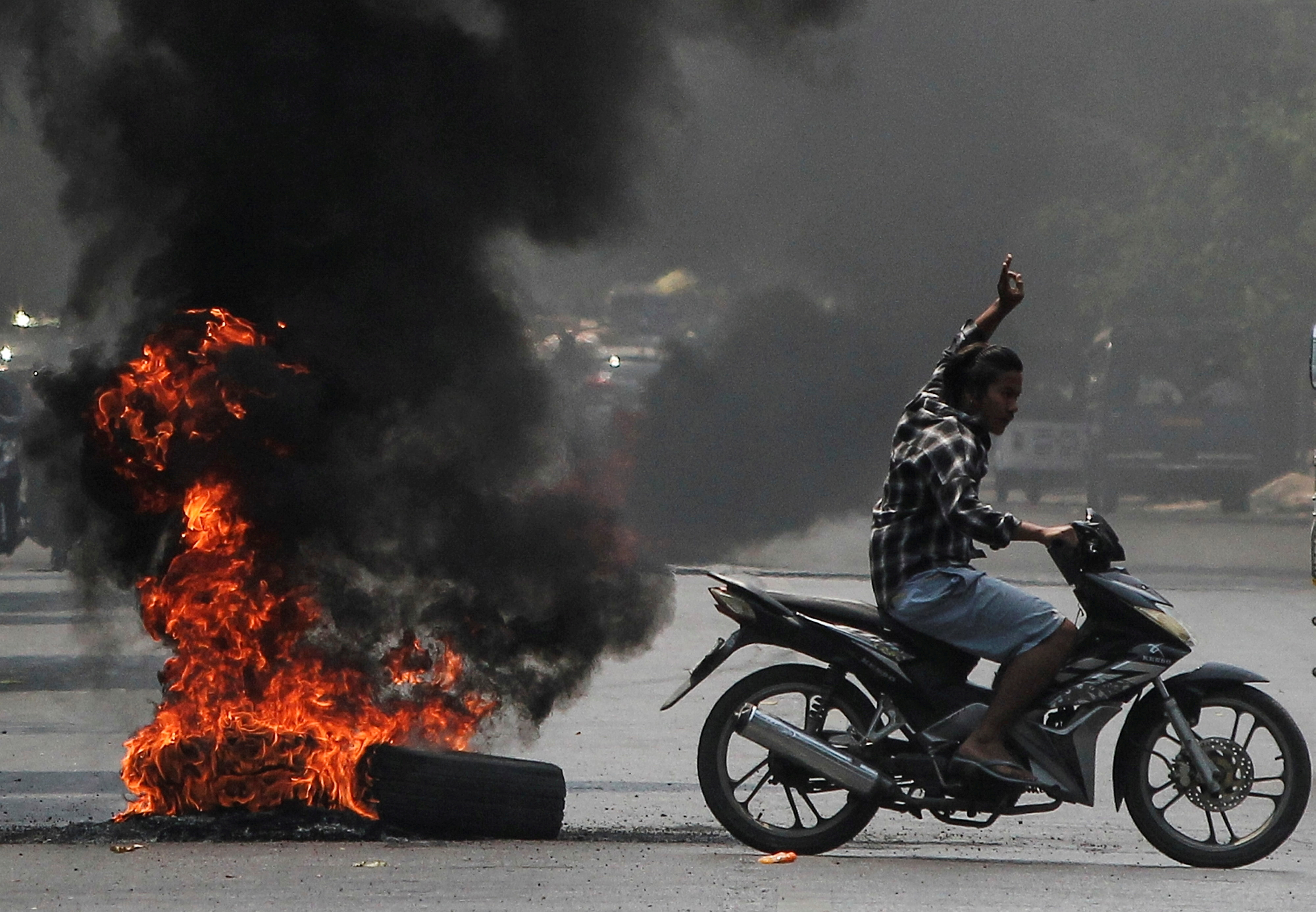 A man flashes the three-finger salute as he passes burning tires during a protest against the military coup, in Mandalay, Myanmar April 1, 2021.