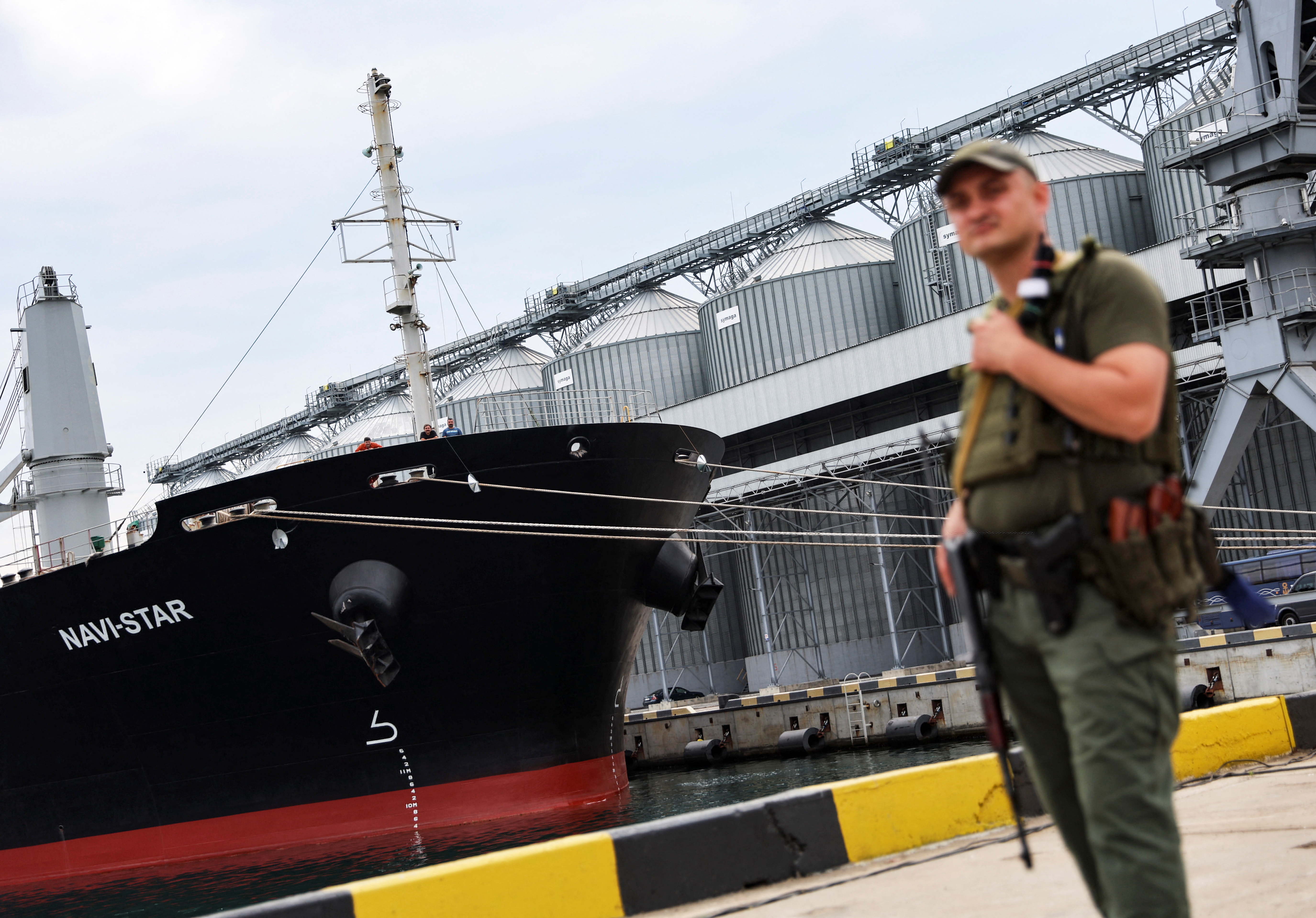 A Ukrainian serviceman in front of silos of grain from Odesa Black Sea port