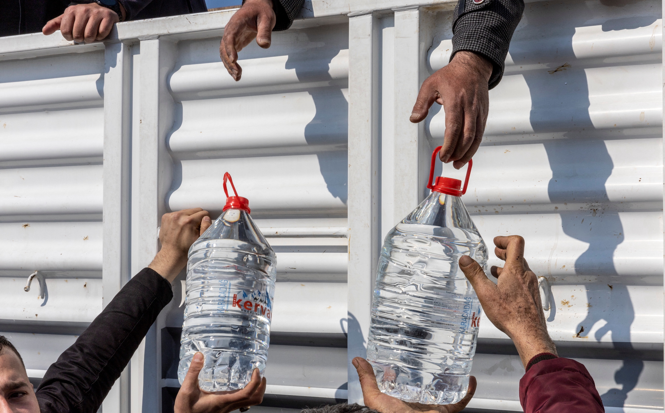 People receive water from aid workers, in the aftermath of the deadly earthquake, in Samandag town of the Hatay province, Turkey