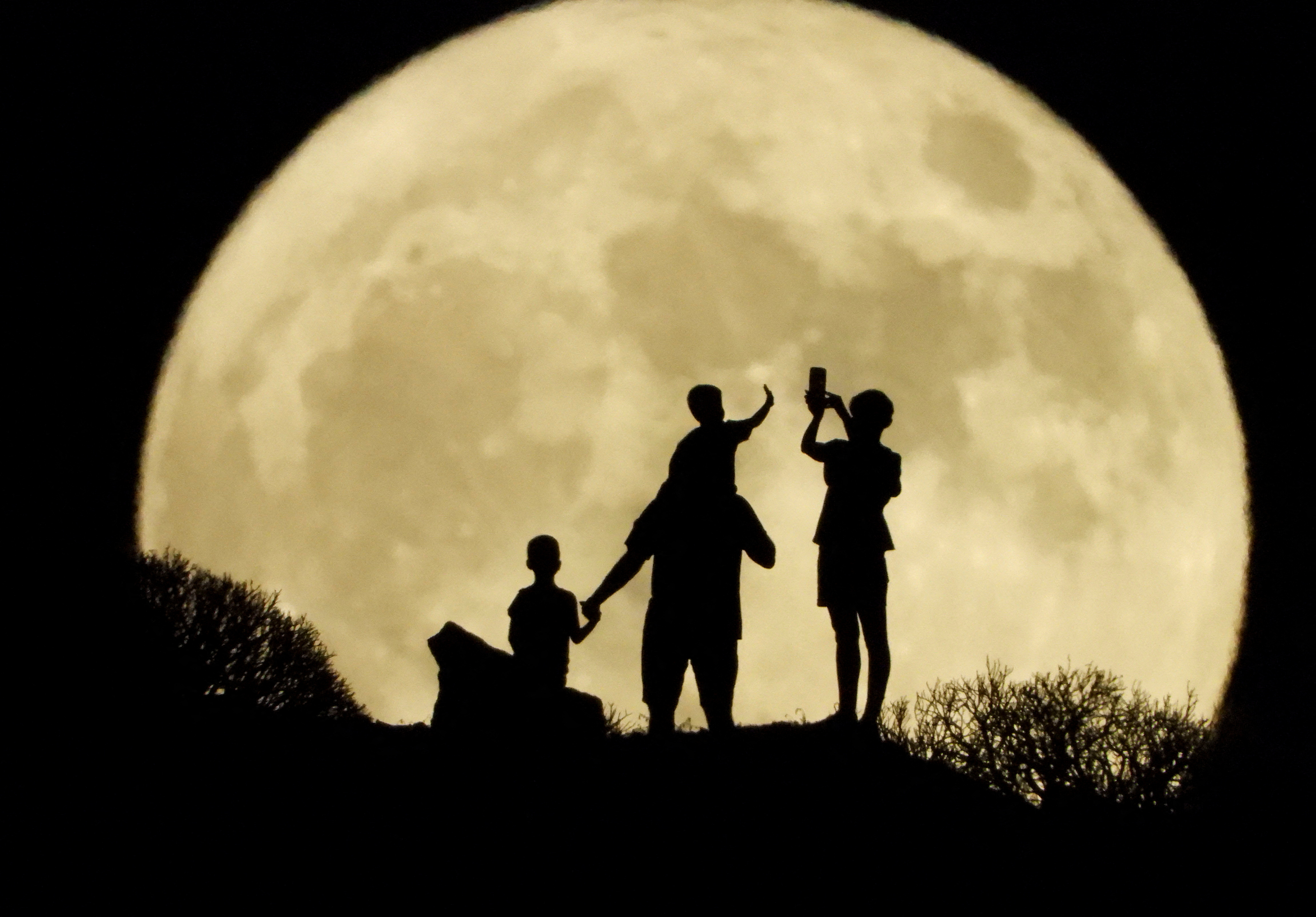 A family stand with the full moon known as the "Sturgeon Moon" in the background, in Arguineguin, in the island of Gran Canaria, Spain