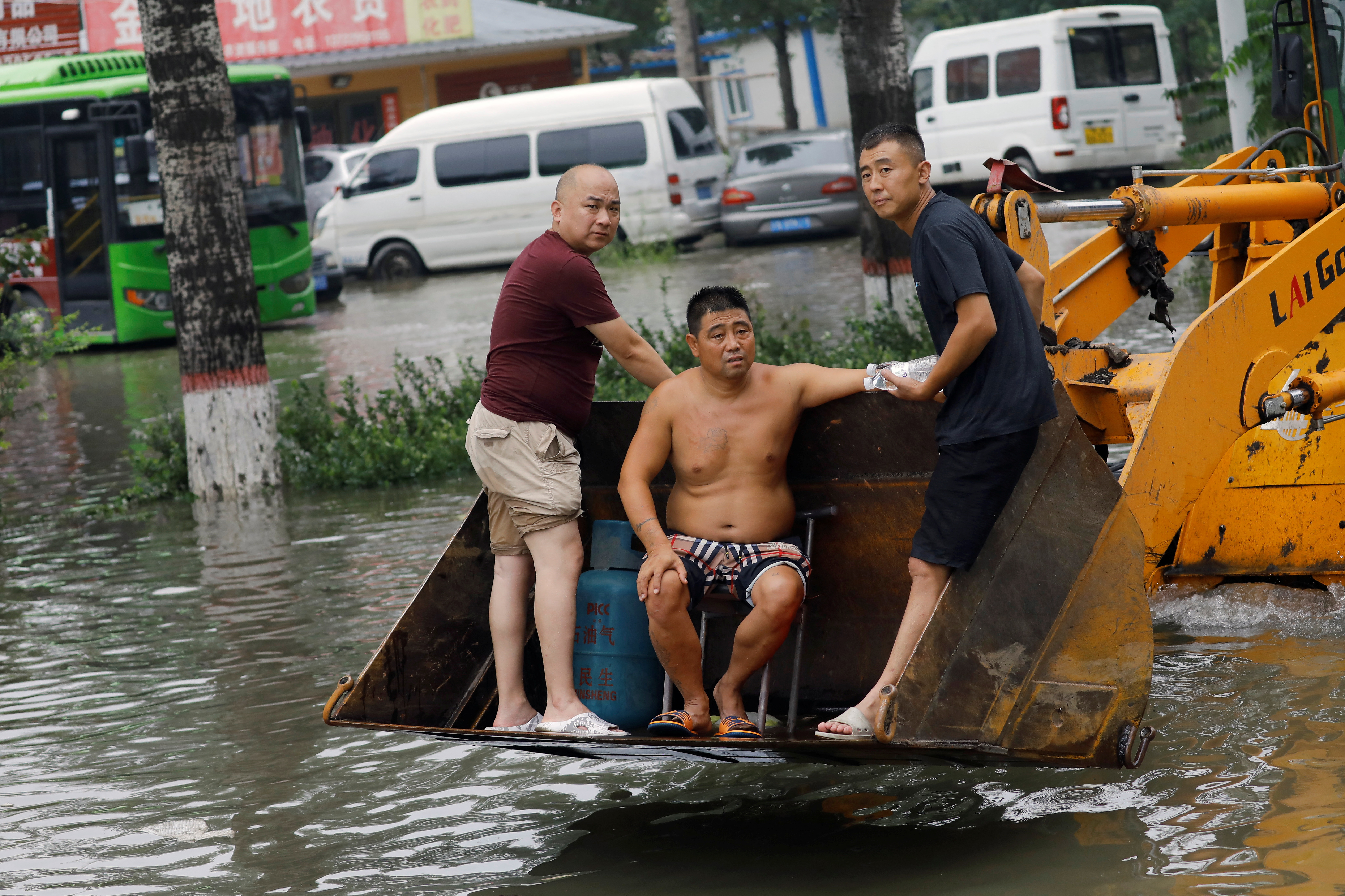 People stand on a front loader travelling through floodwaters after the rains and floods brought by remnants of Typhoon Doksur