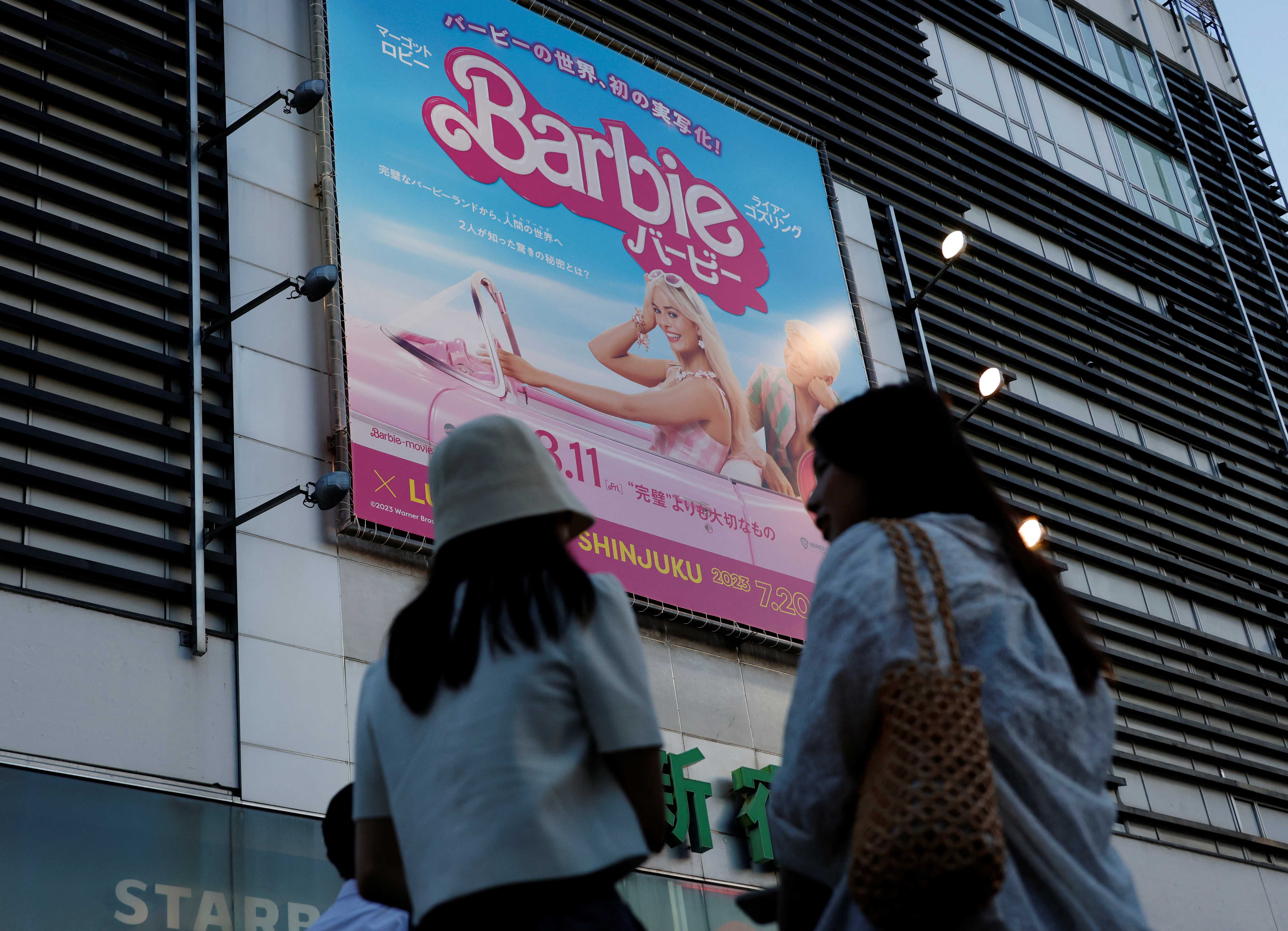 Women stand in front of a promotional poster of film "Barbie" in Tokyo, Japan, August 3, 2023. REUTERS/Kim Kyung-Hoon