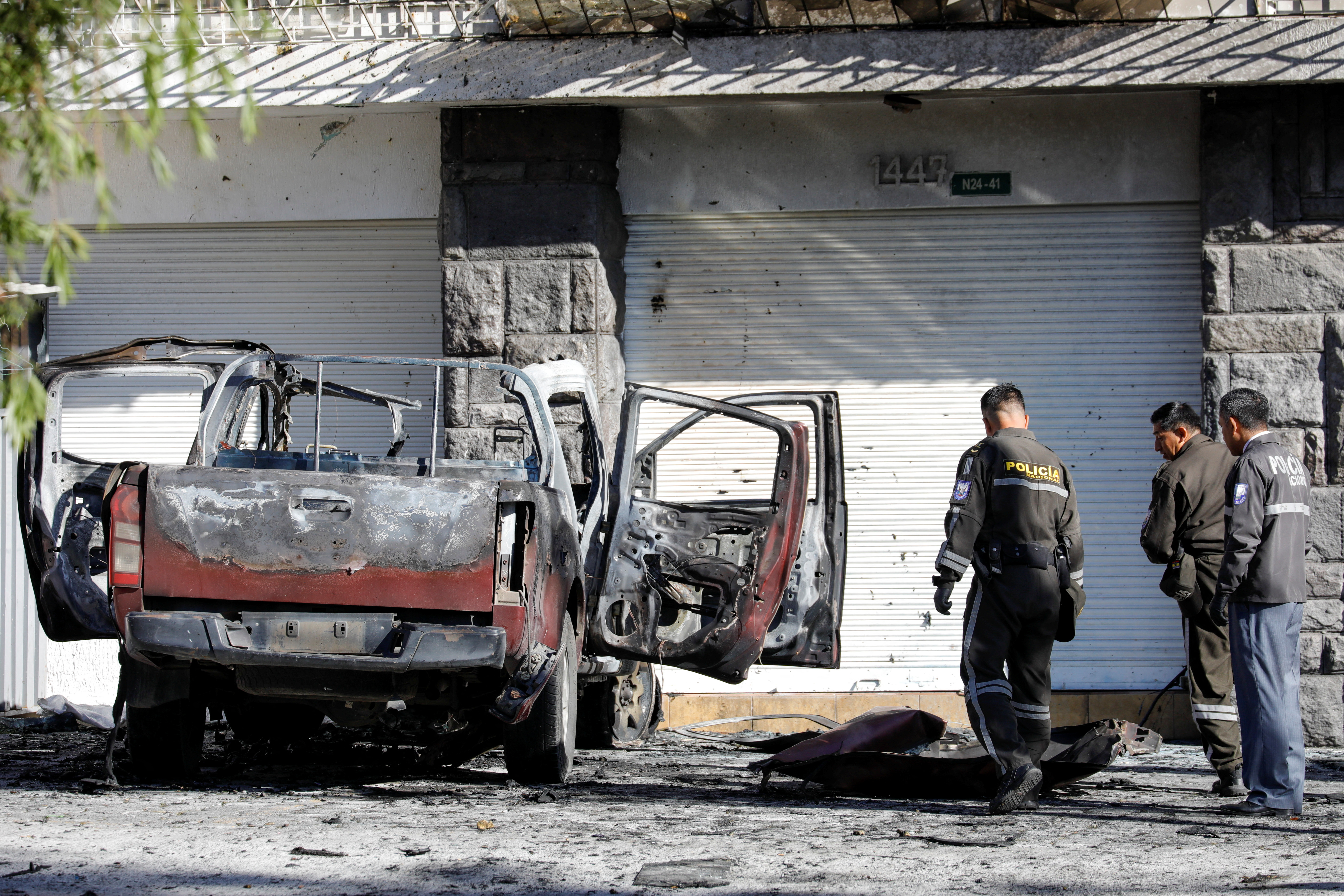Police officers check the remains of a car after a car bomb exploded in Quito, Ecuador