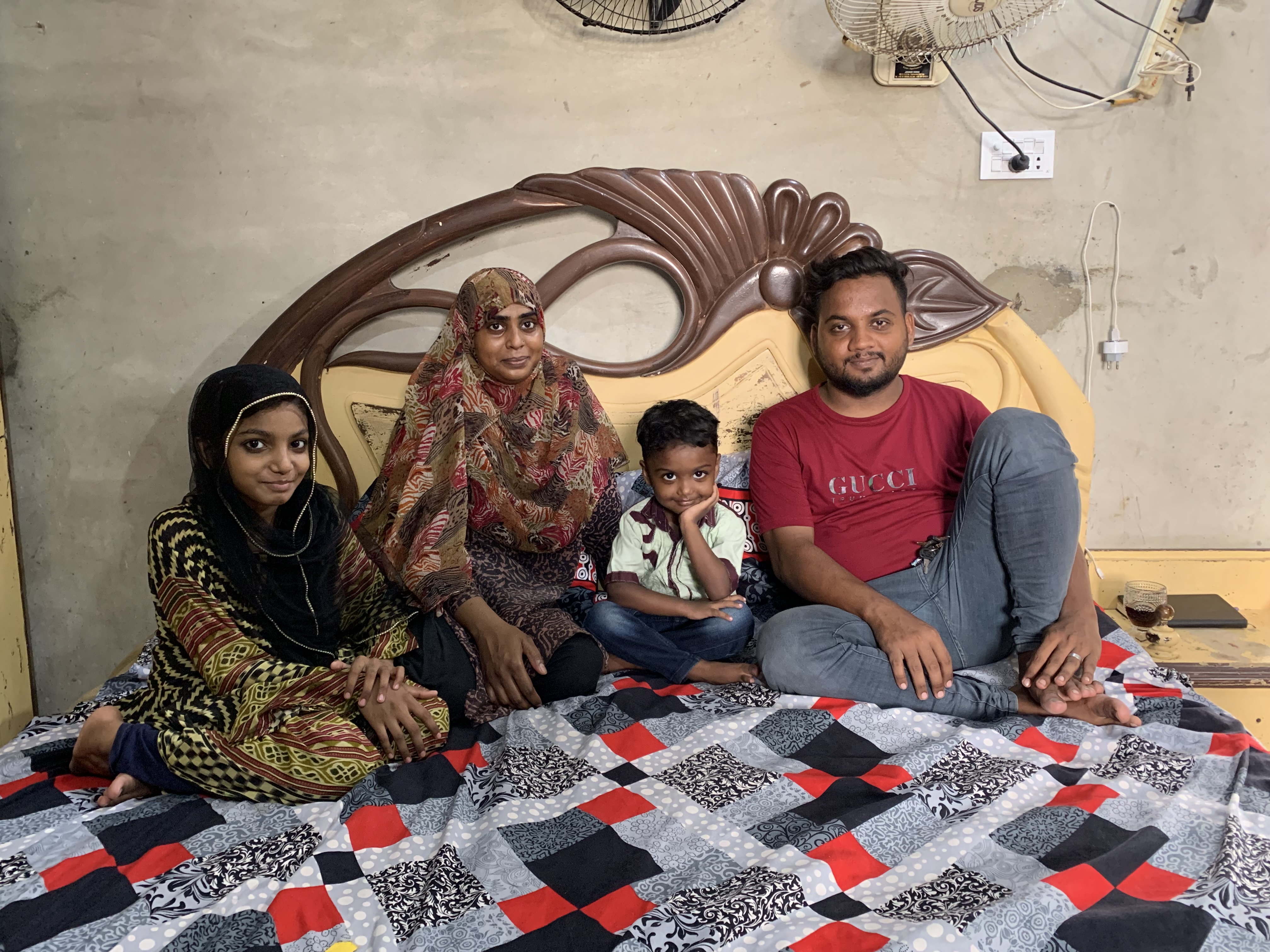 A photo of a family of four sitting on a bed.