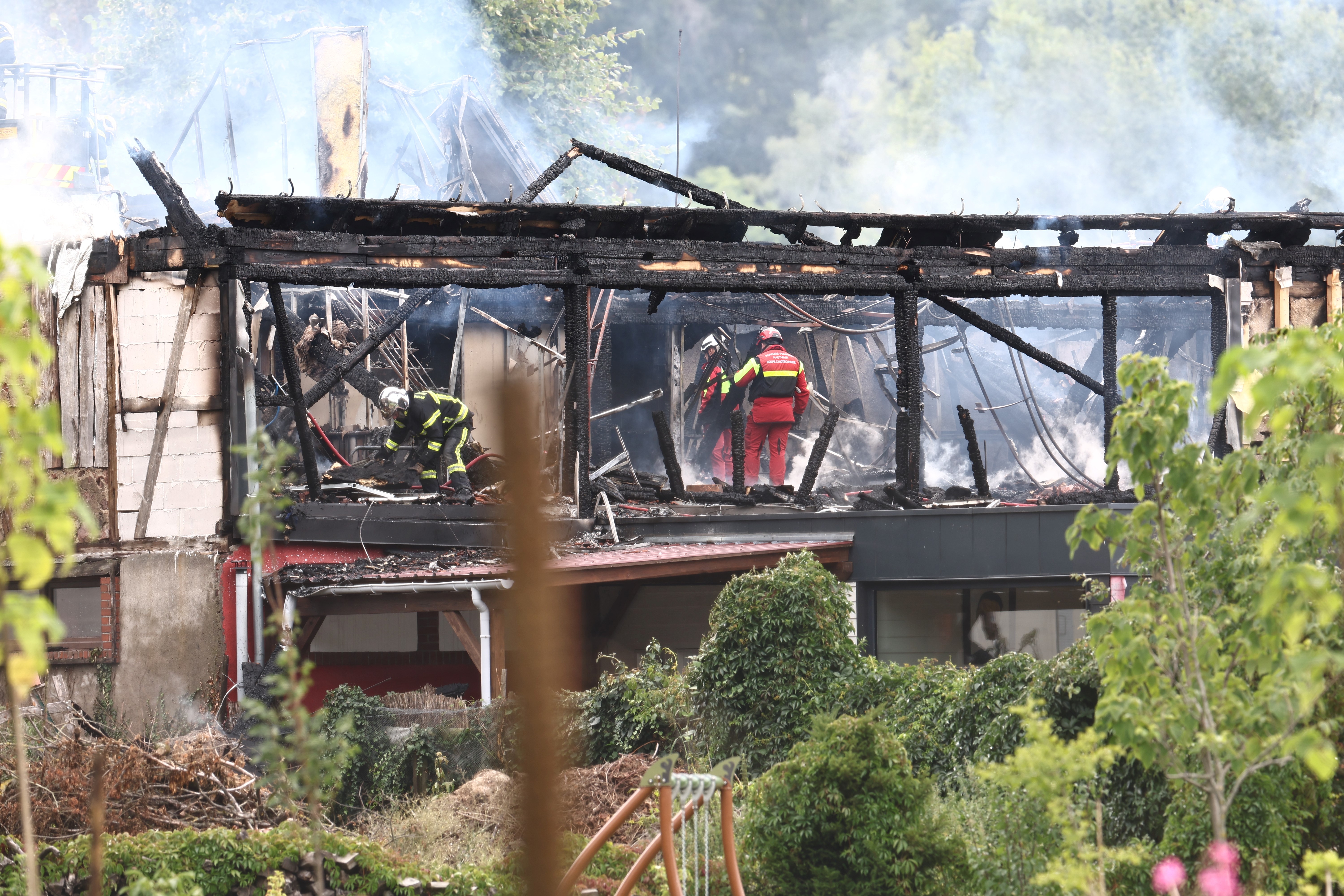 Firefighters inspect a burnt building after a fire erupted at a holiday home for disabled people in Wintzenheim, eastern France