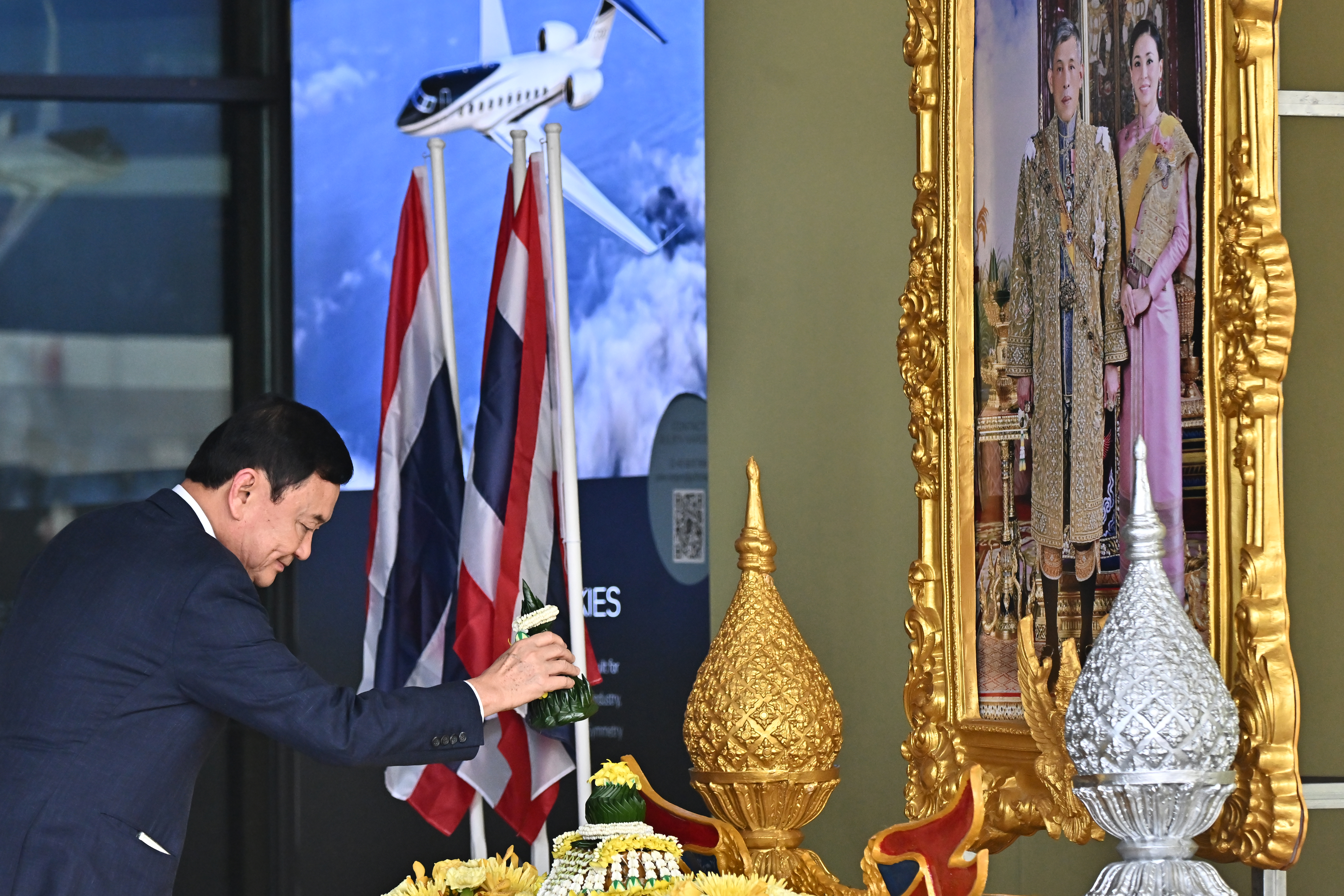 Thaksin prepares to bow in homage to the Thai king's portrait. The picture is on the right. There are urns, flowers and flags.