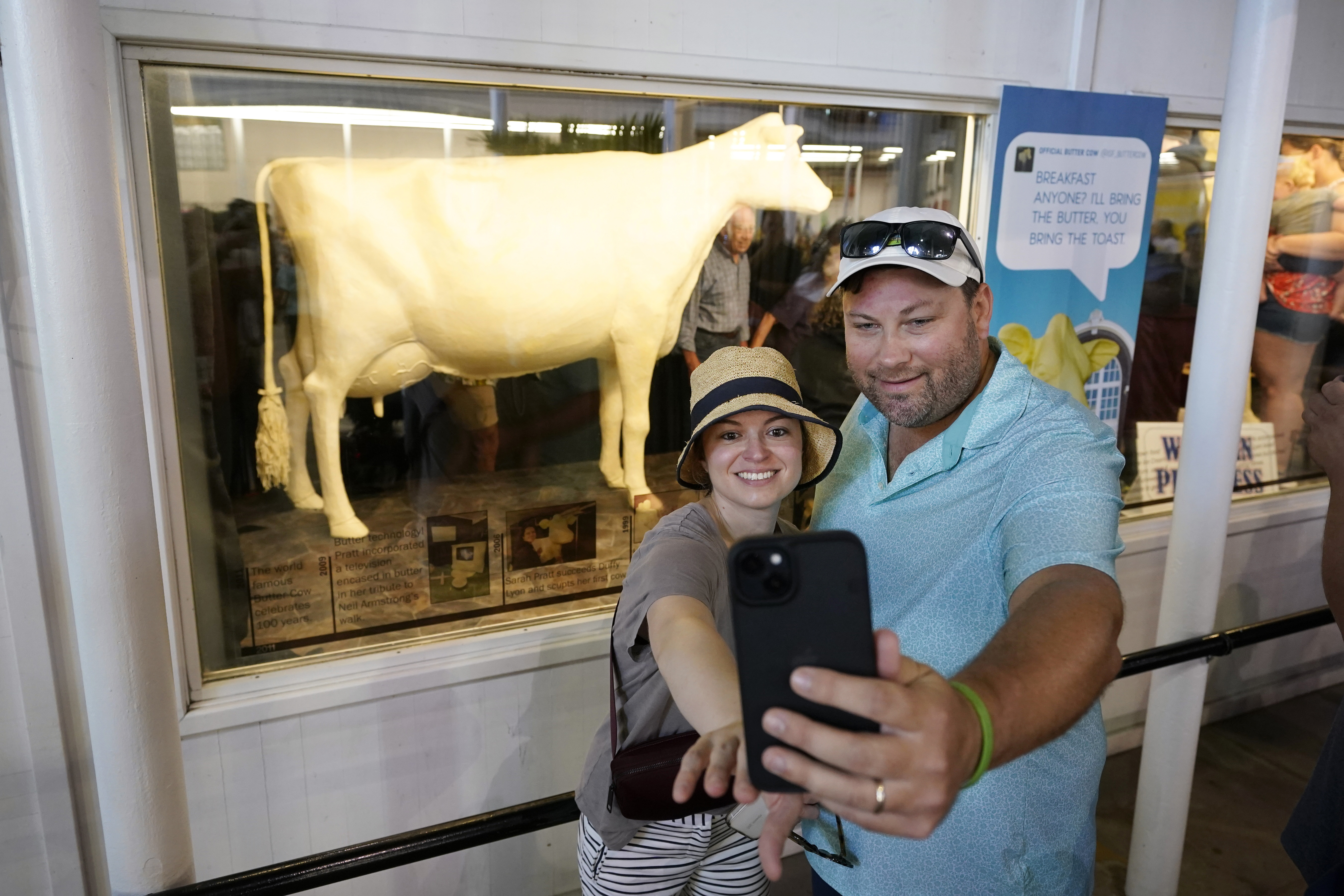A couple poses for a selfie in front of a cow sculpted from butter.