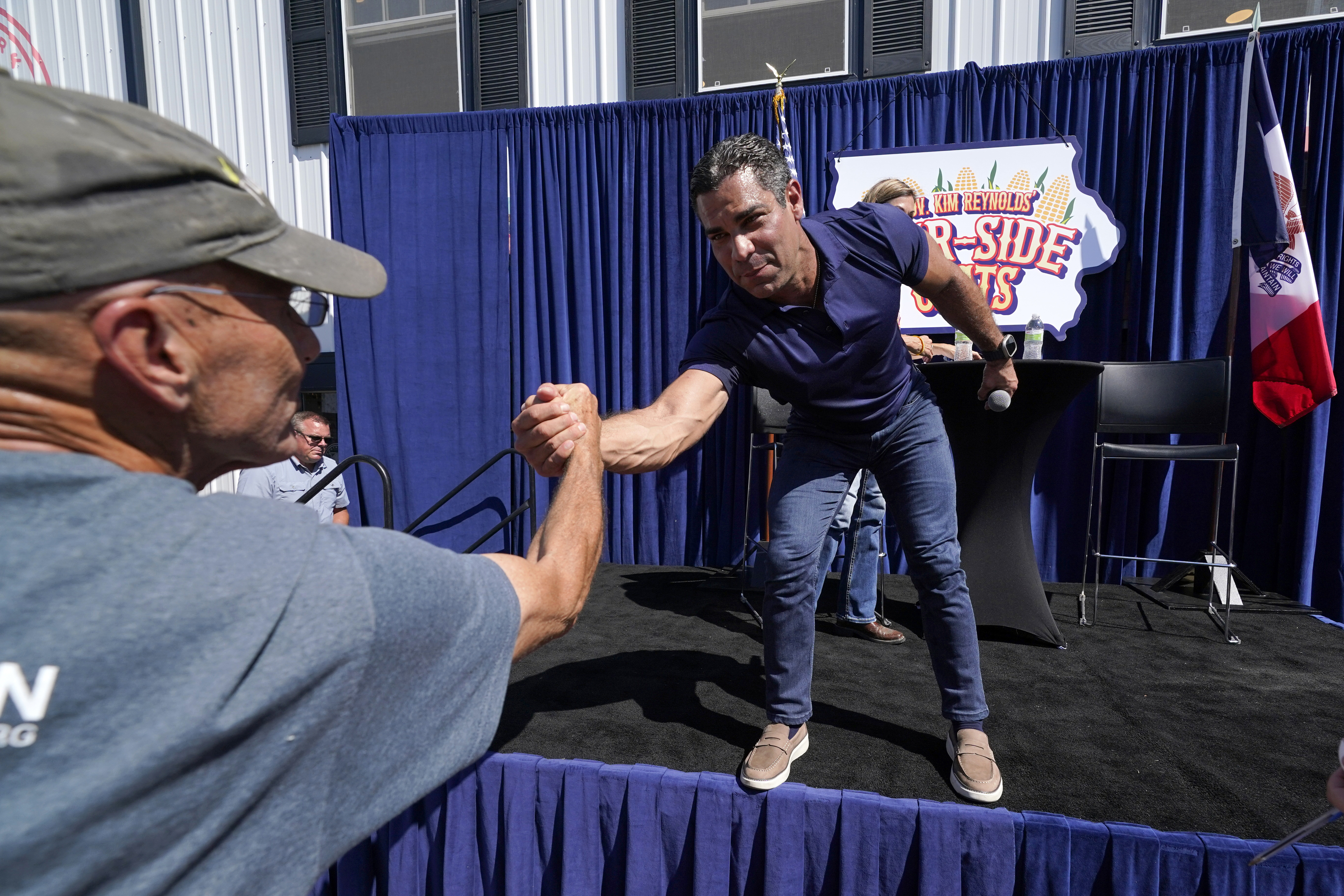 Francis Suarez, wearing jeans and a polo shirt, reaches to shake hands with a fan, as he leans down from the stage of the Fair-Side Chat.