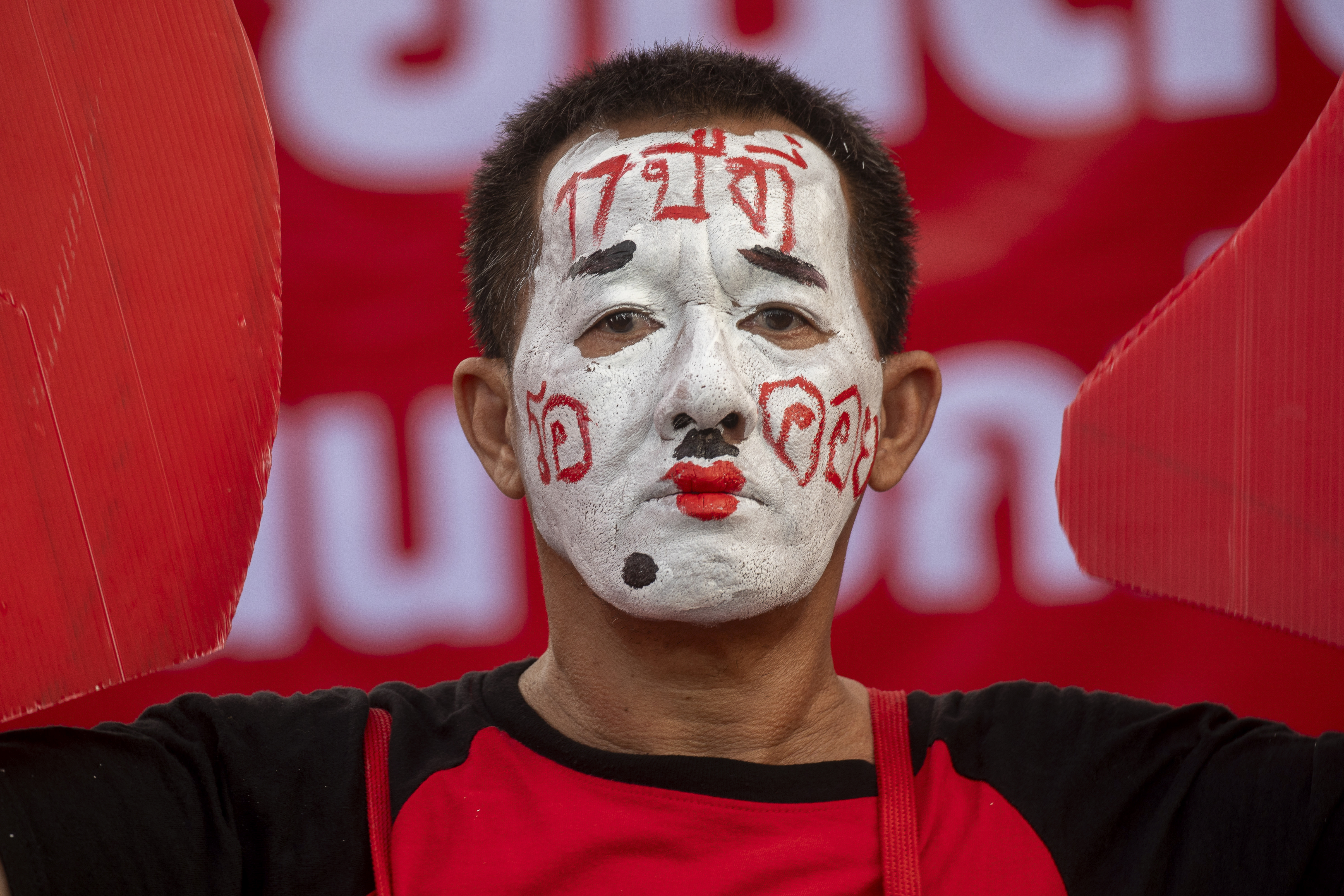 A Thaksin supporter with his face painted waits for the former PM to return. His face is white with red writing on his forehead and cheeks. 