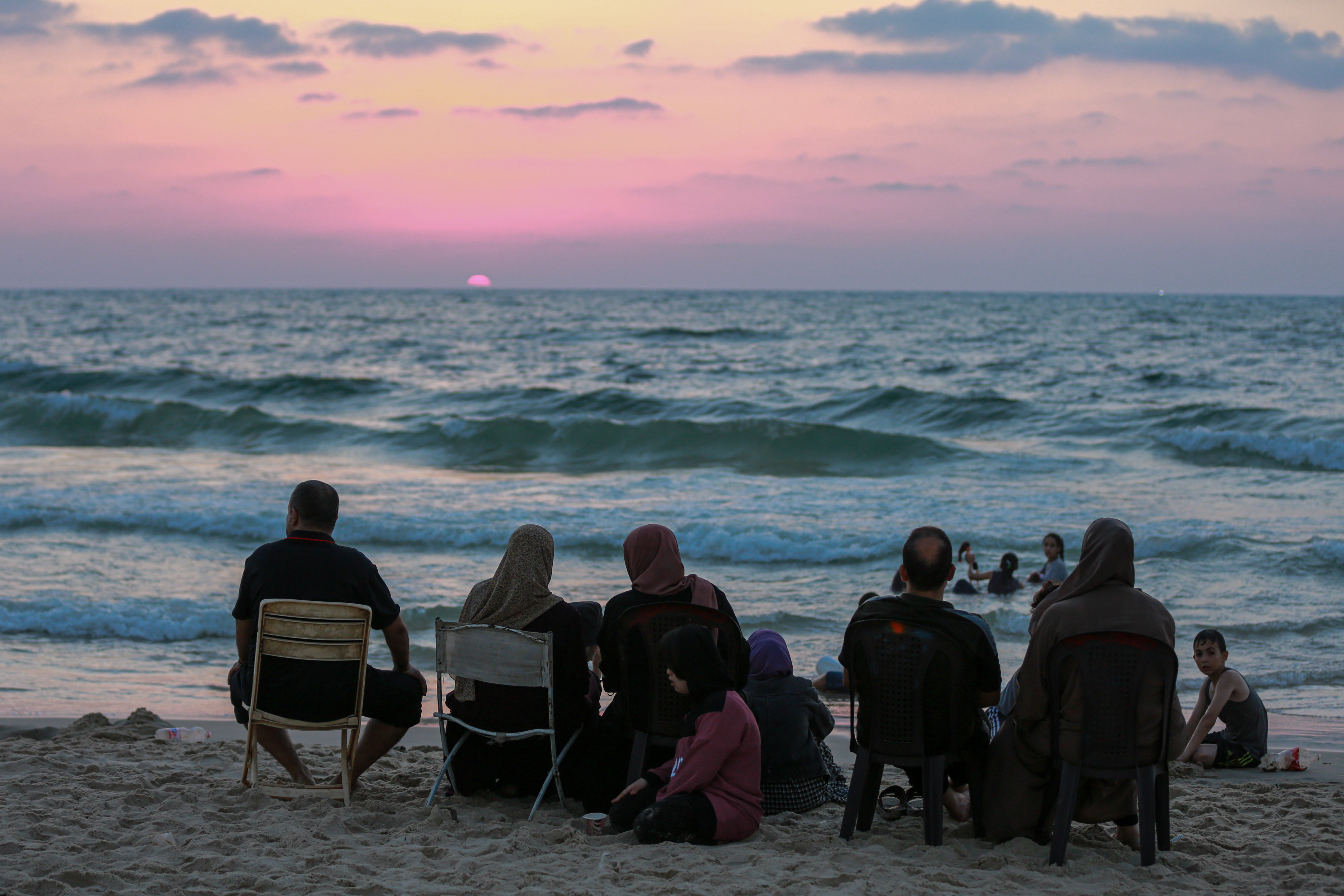a family seated looking at the waves as the sun sets