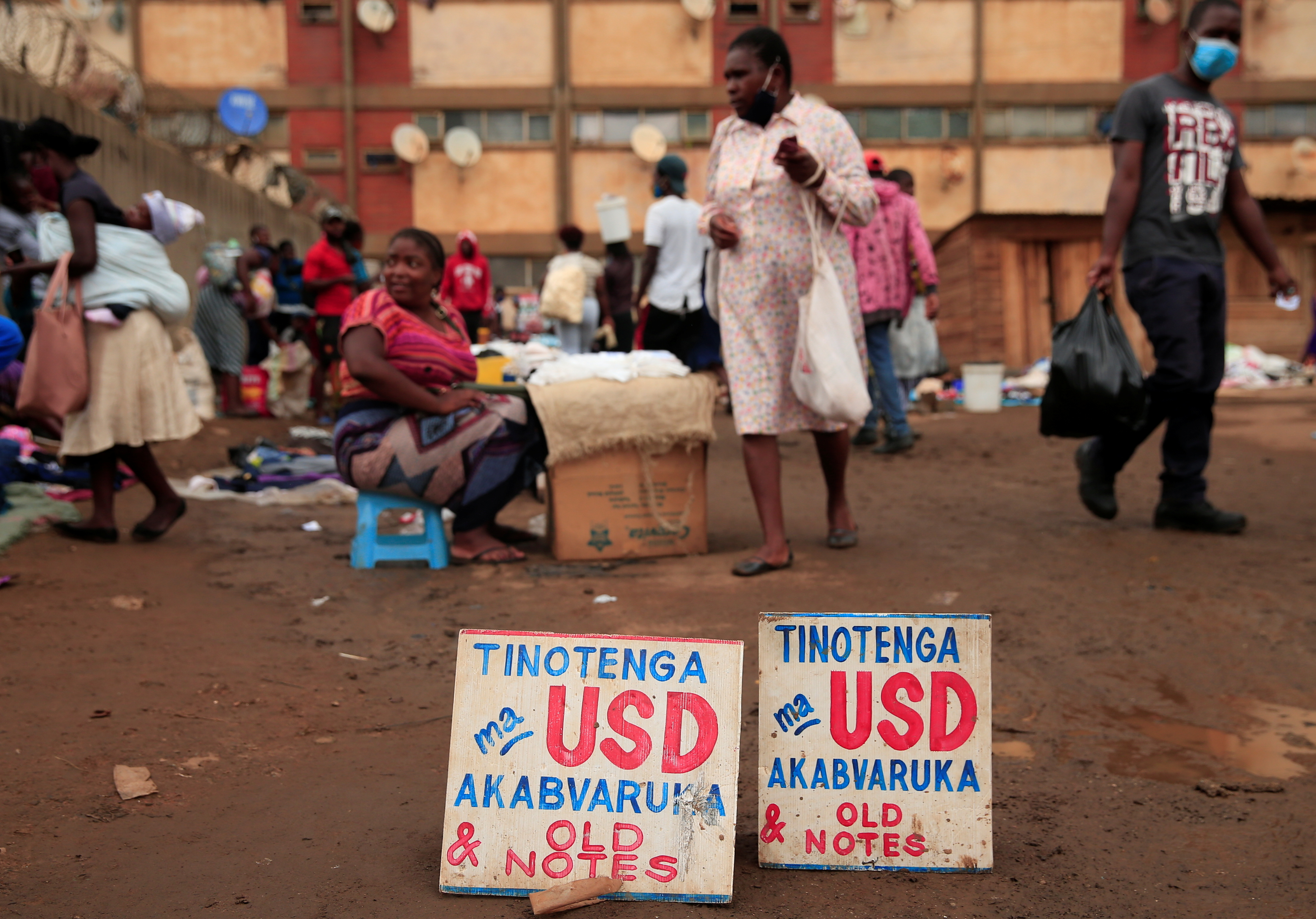 People walk past a money-changers sign at a market in Harare