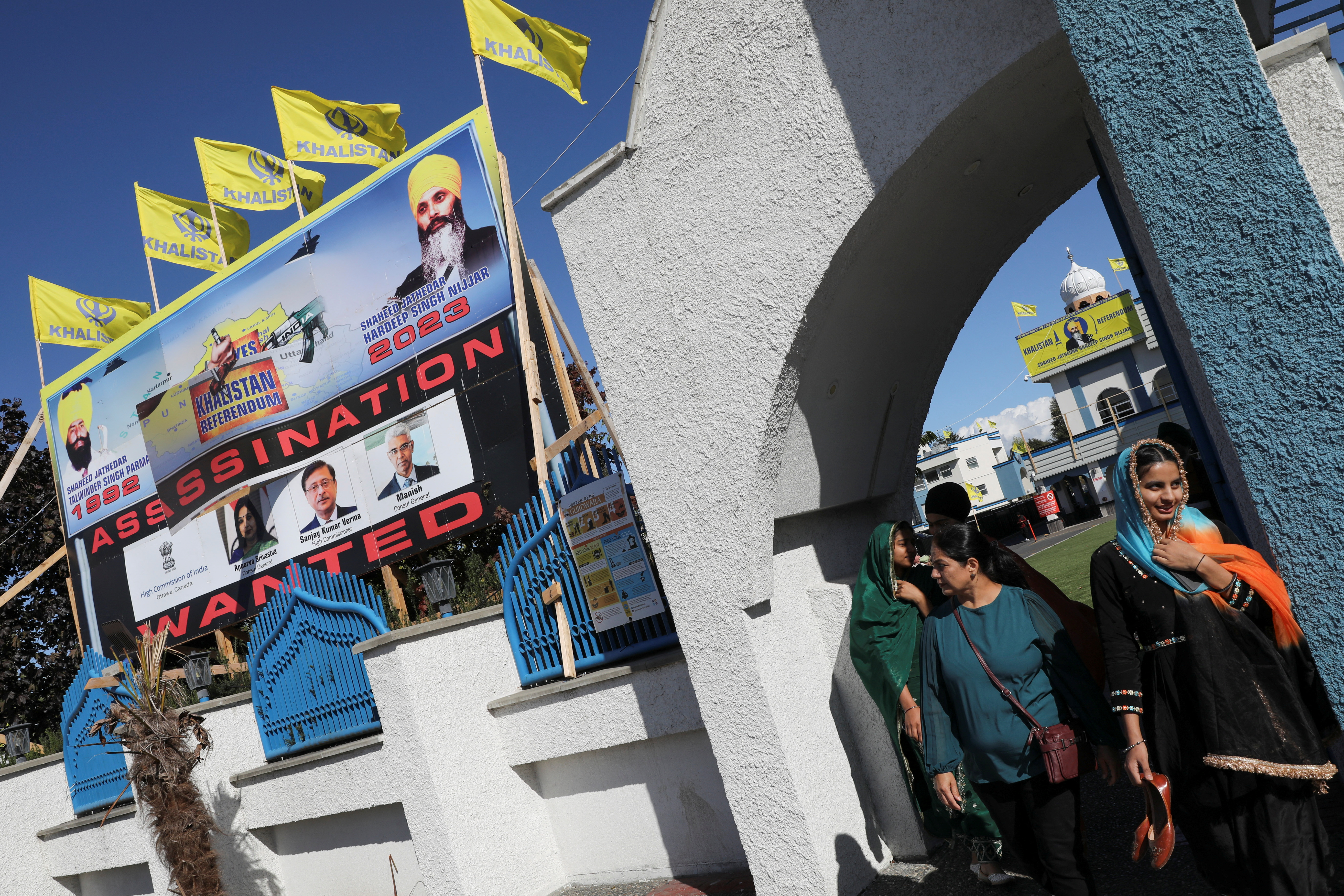 People walking out of the Guru Nanak Sikh temple where Hardeep Singh Nijjar, was killed in June. There's a large banner about his 'assassination' and yellow flags flying above