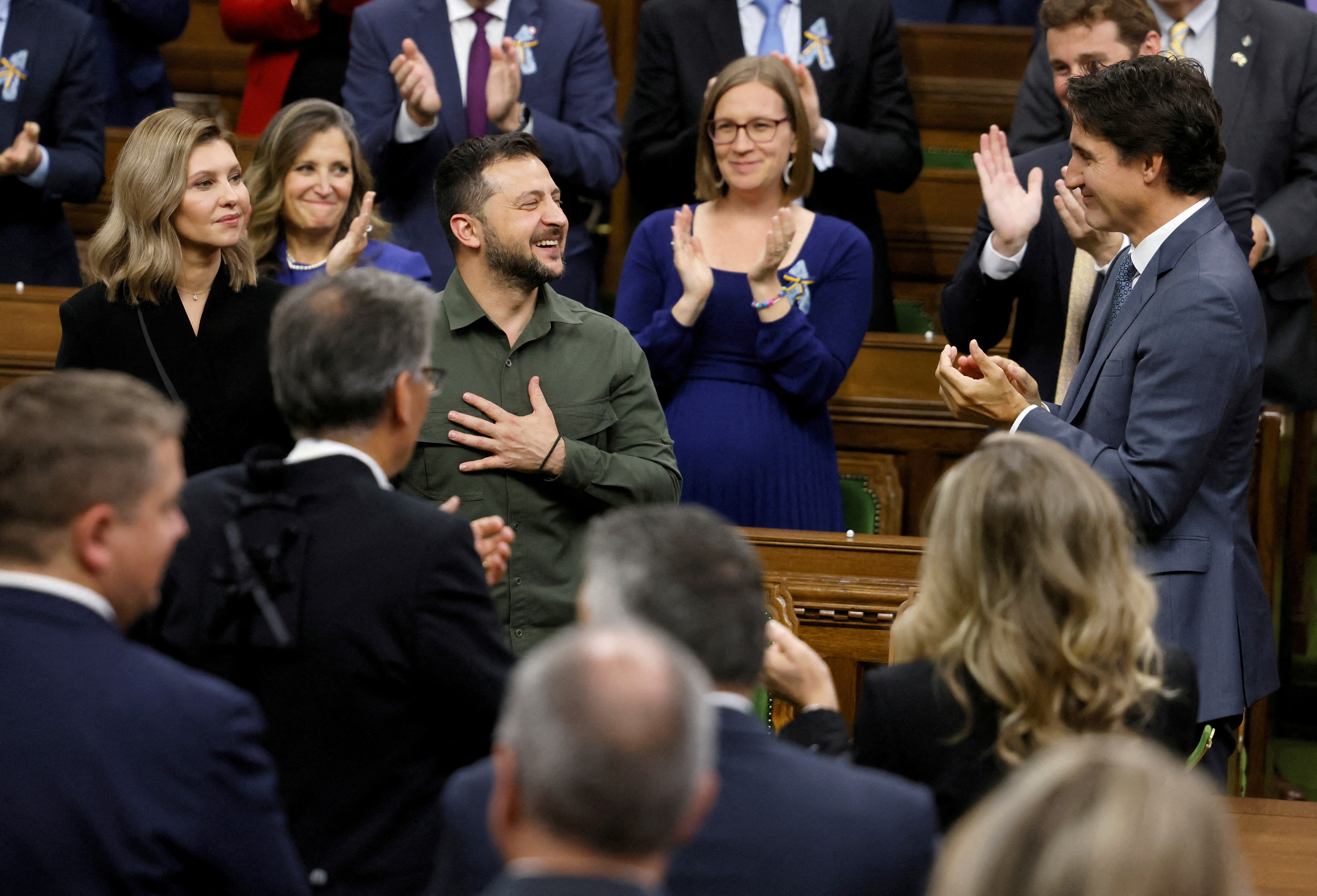 Volodymyr Zelenskyy puts a hand over his heart and smiles as Justin Trudeau and members of Canada's Parliament applaud him on the floor of the House of Commons.